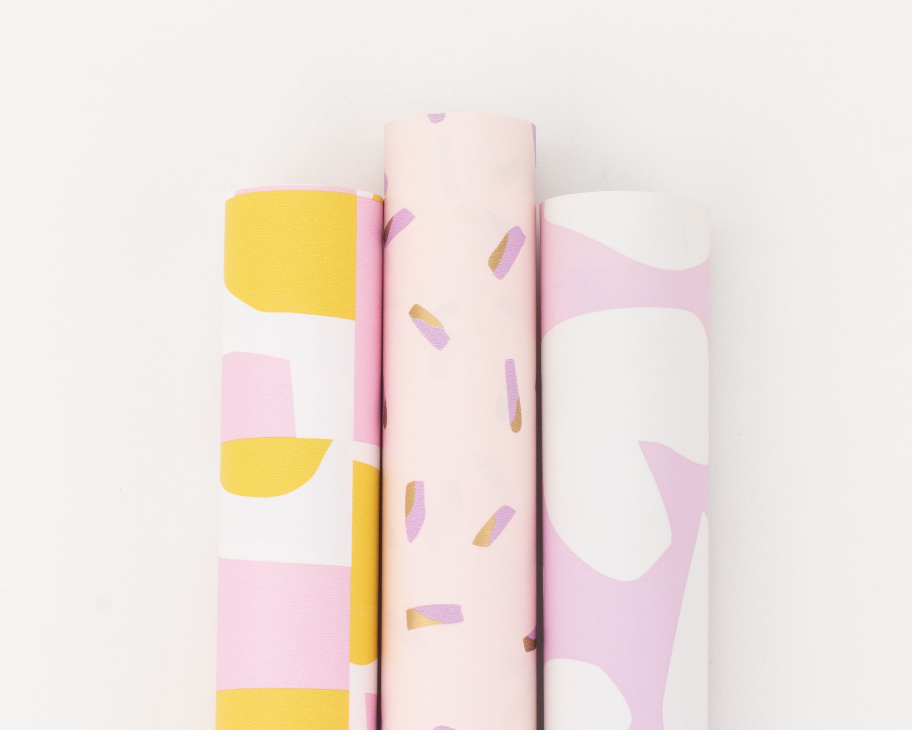 Geschenkpapier-Set mit drei Rollen in Rosa, Flieder, Gelb und Gold, von oben fotografiert. Die Rollen zeigen Pastellmuster
