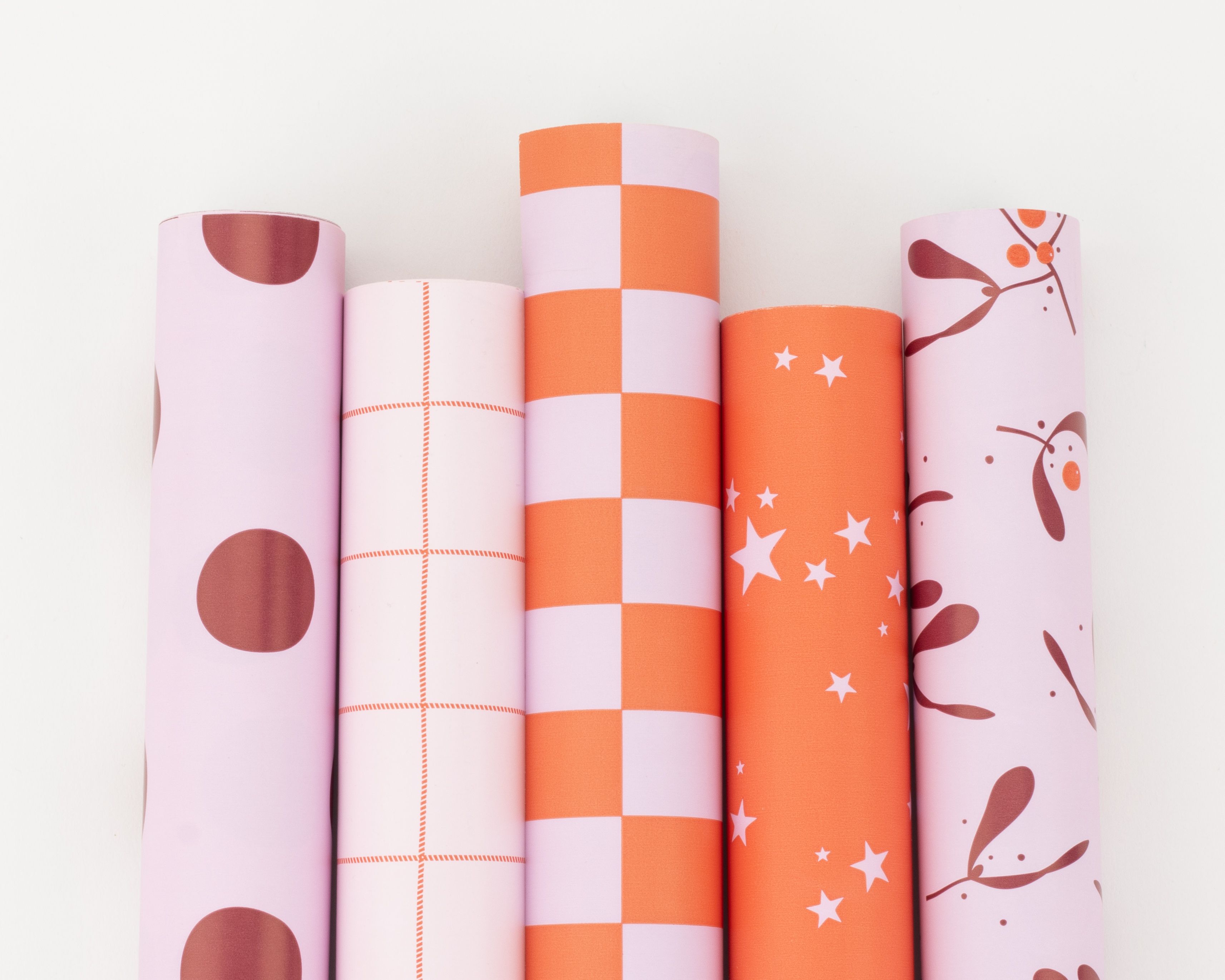 Geschenkpapier-Set mit fünf Rollen in Hellrosa, Orangerot und Weinrot mit festlichen Mustern wie Punkten, Blockstreifen und Sternen