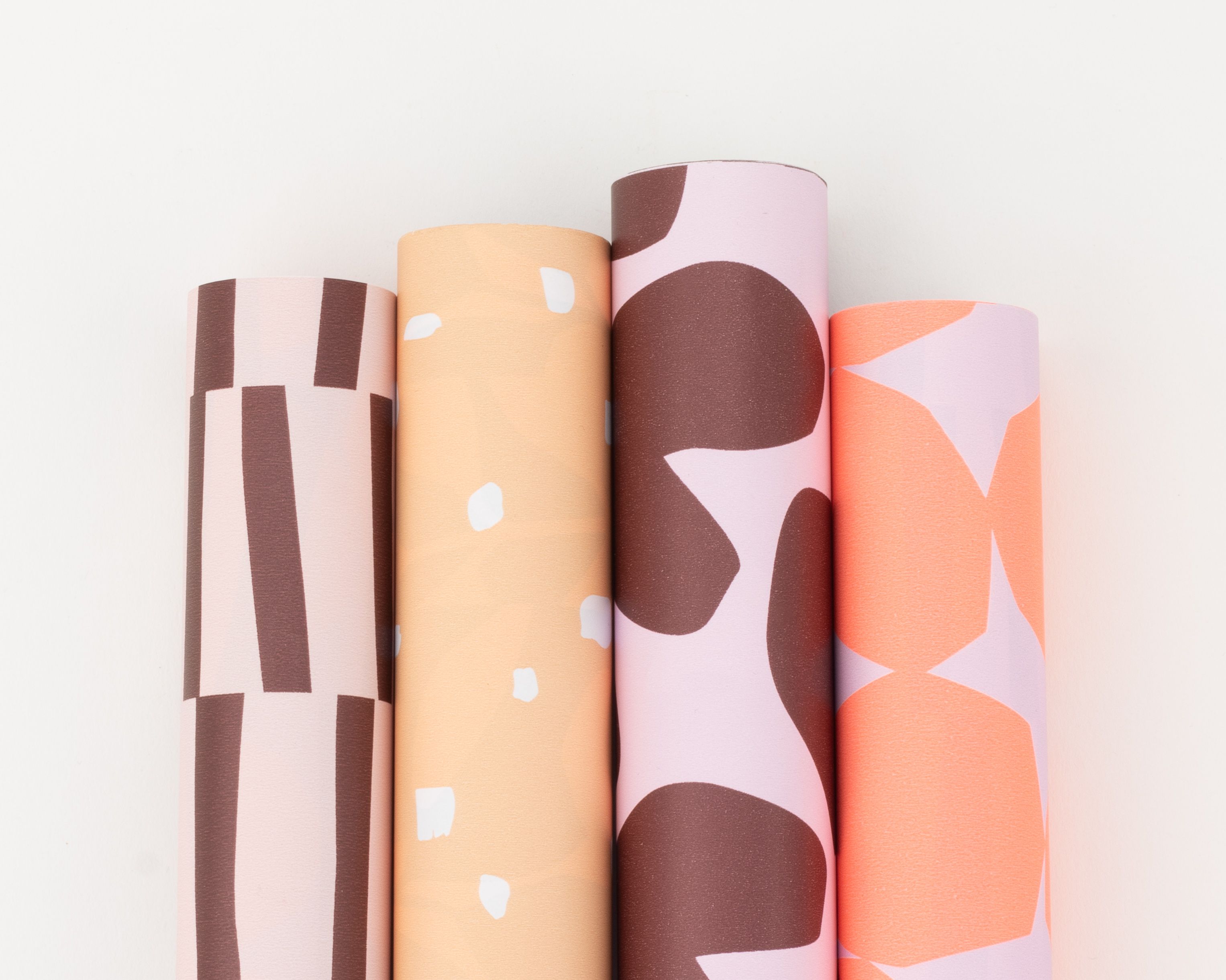 Geschenkpapier-Set mit vier Rollen in weinrot, rosa, peach und neonorangerot. Die Designs umfassen Streifen, Punkte und Herzmotive
