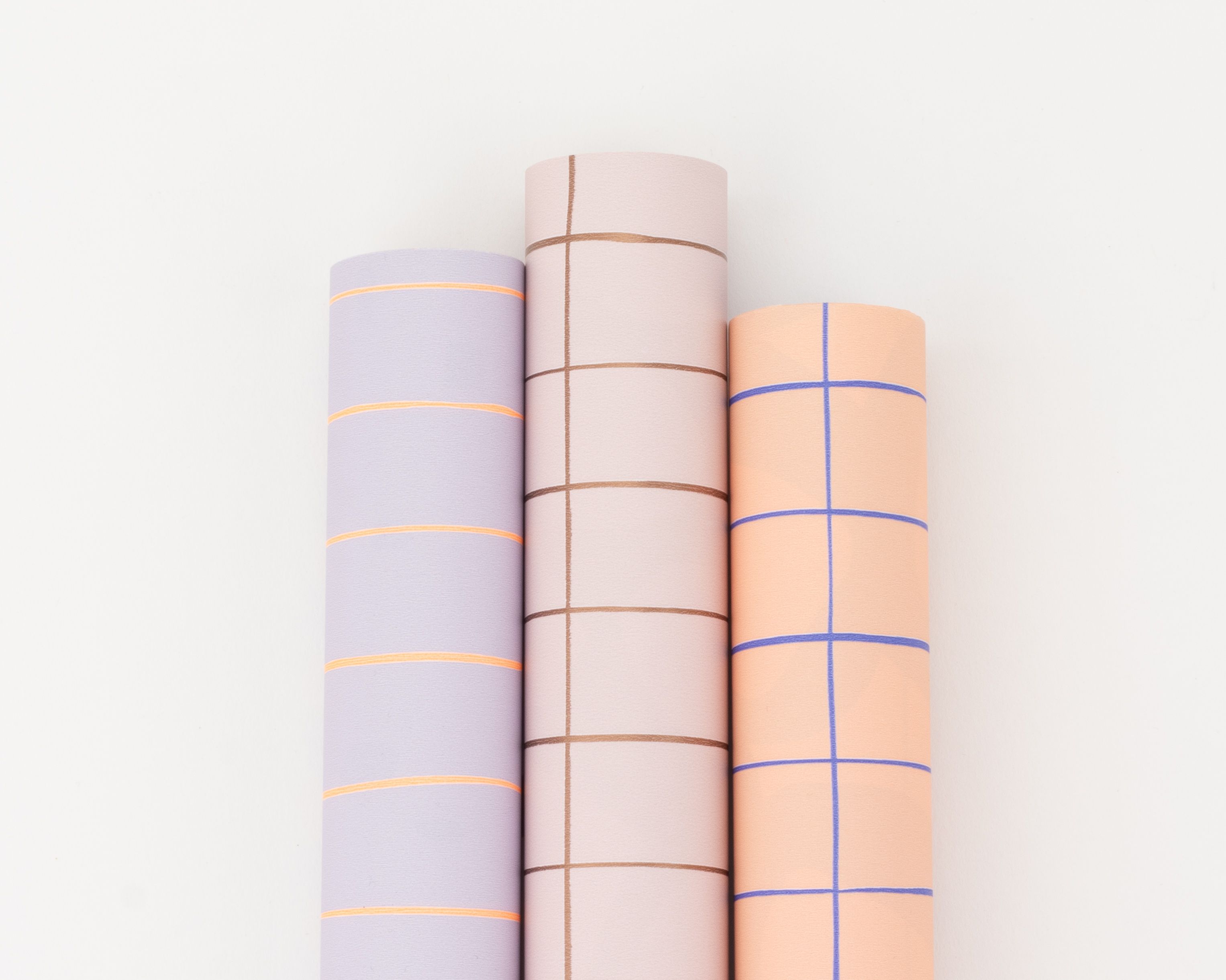 Geschenkpapier-Set mit drei Rollen, nebeneinander liegend, in den Farben Flieder, Rosa und Orange, jeweils mit einem Rasterdesign