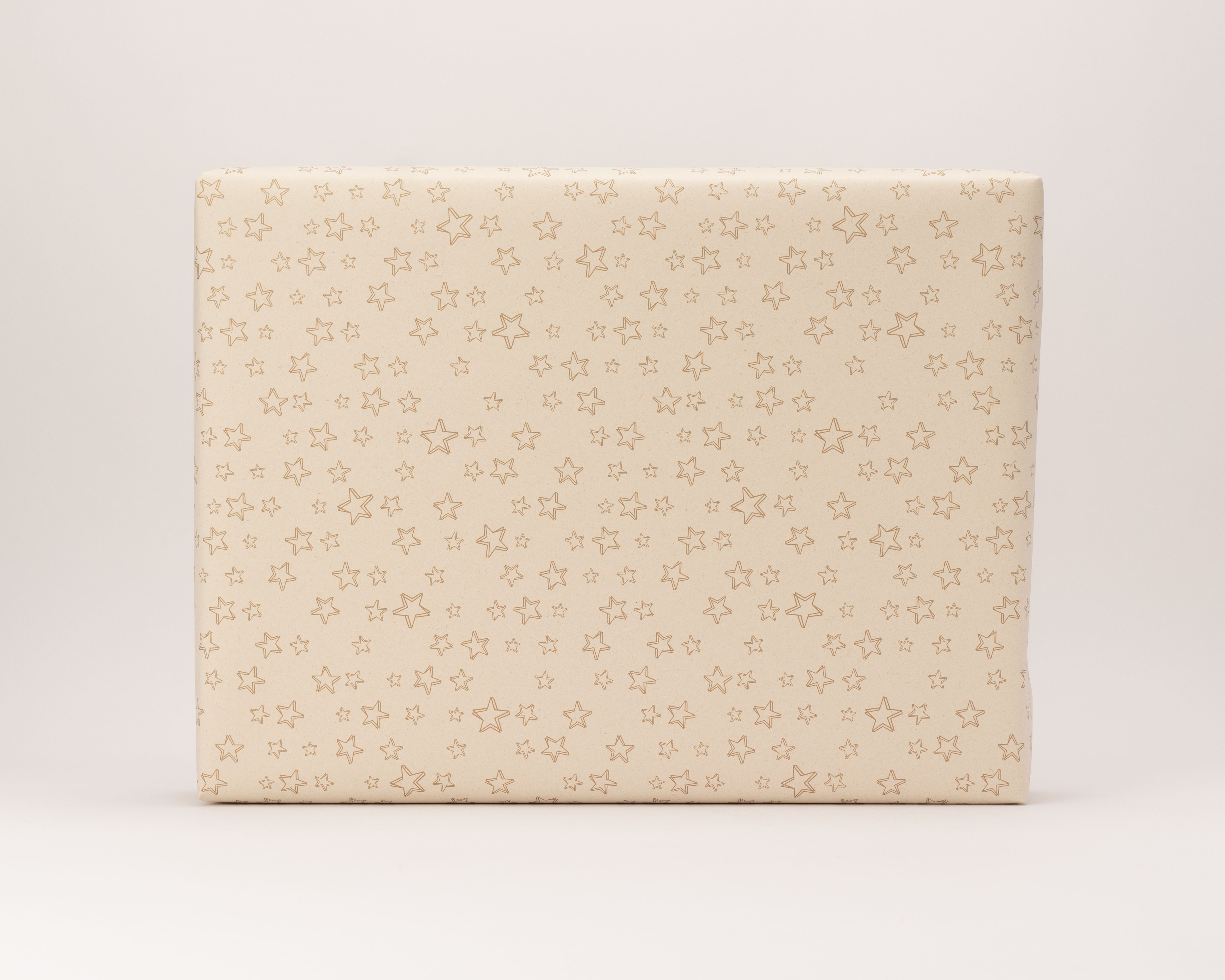 Geschenkpapier-Set, ein damit verpacktes Geschenk in hellem Kraftpapier. Das Papier zeigt ein Muster aus goldenen Umriss-Sternen