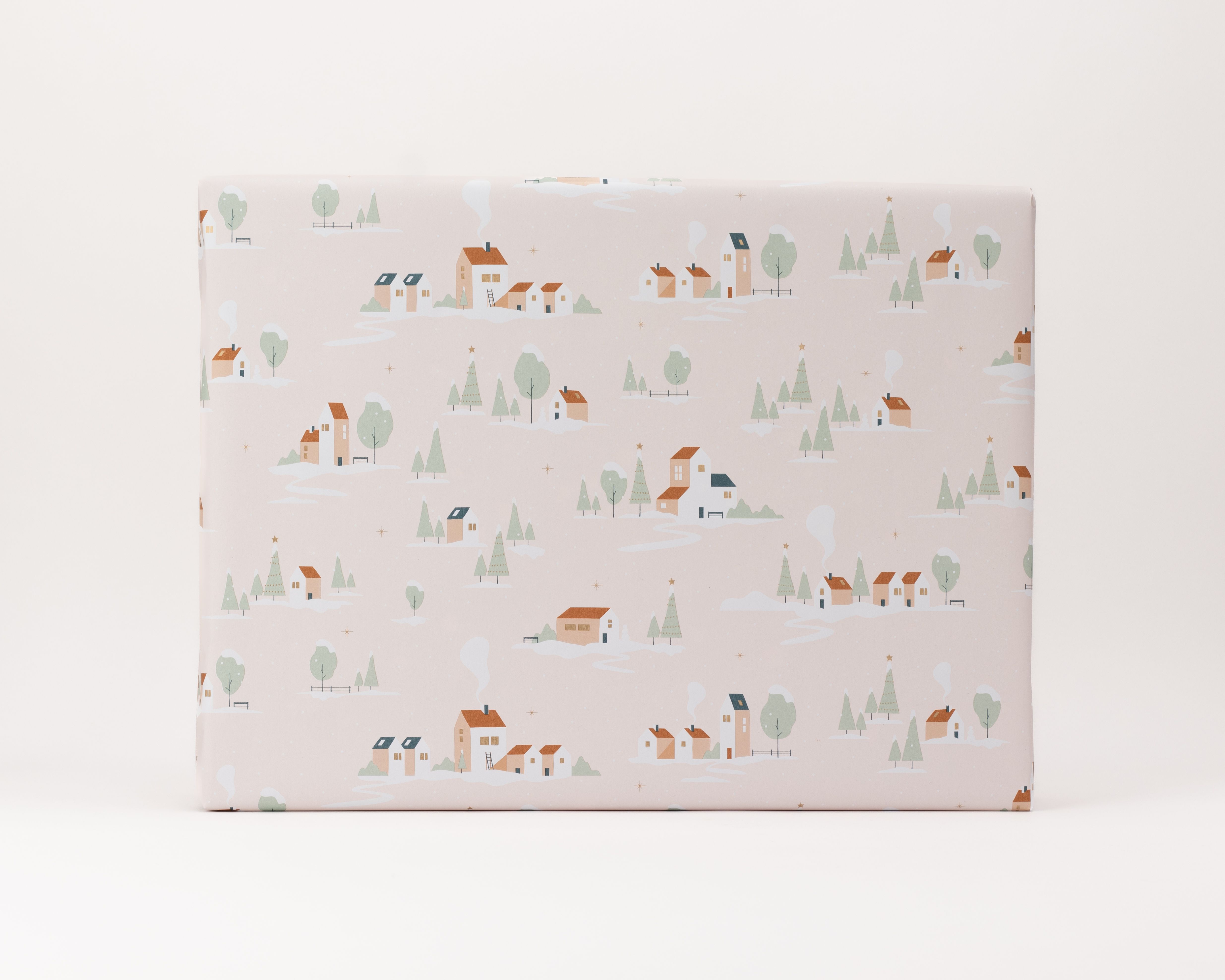 Geschenkpapier-Set mit einem Geschenk, eingewickelt in zartrosa Papier, das ein Muster aus stilisierten Winterdorf-Häusern, Bäumen und Bänken zeigt.