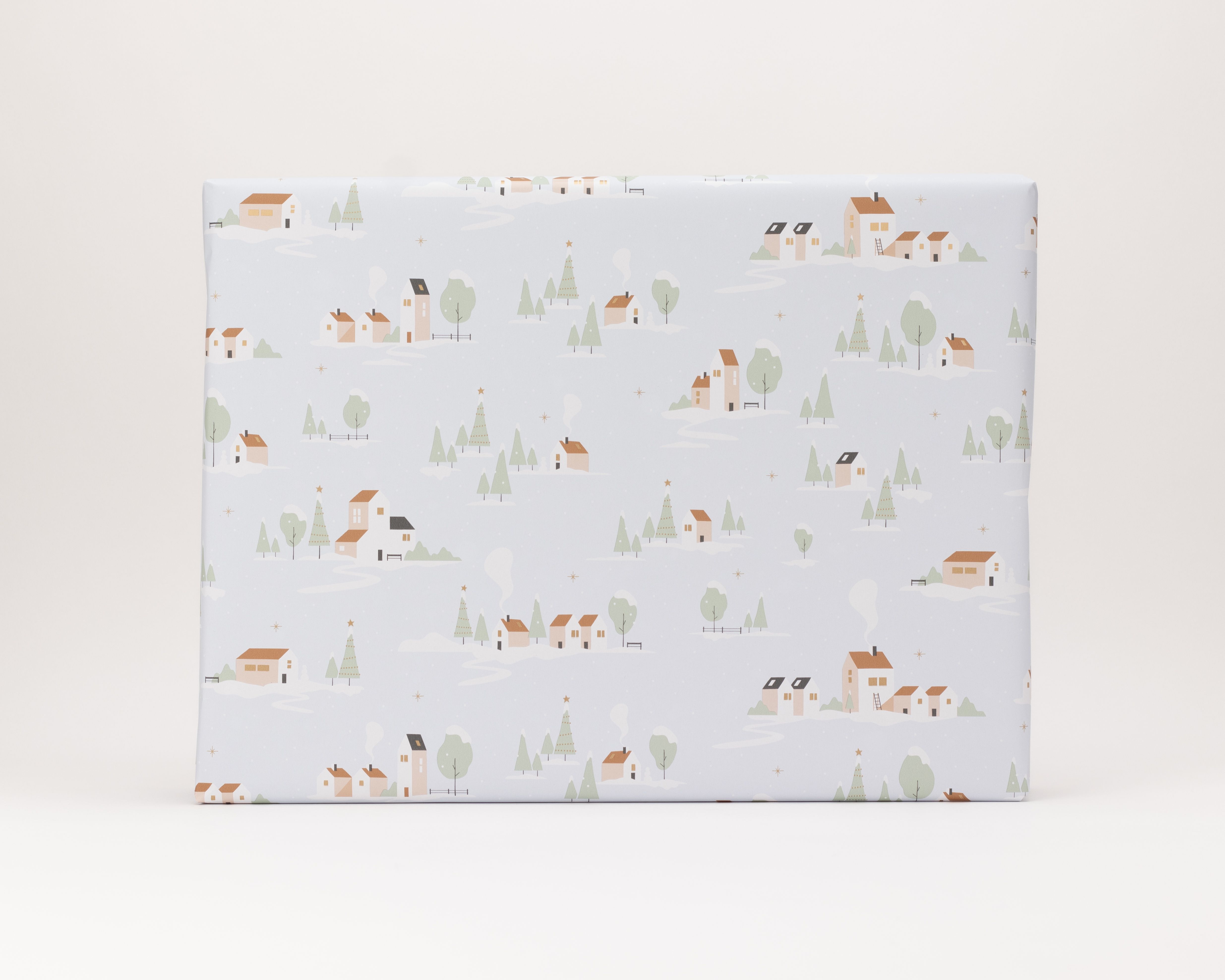 Geschenkpapier-Set mit einem verpackten Geschenk in hellem Blauton. Das Papier zeigt ein winterliches Dorfmotiv mit Häusern, Bäumen und Schneelandschaft
