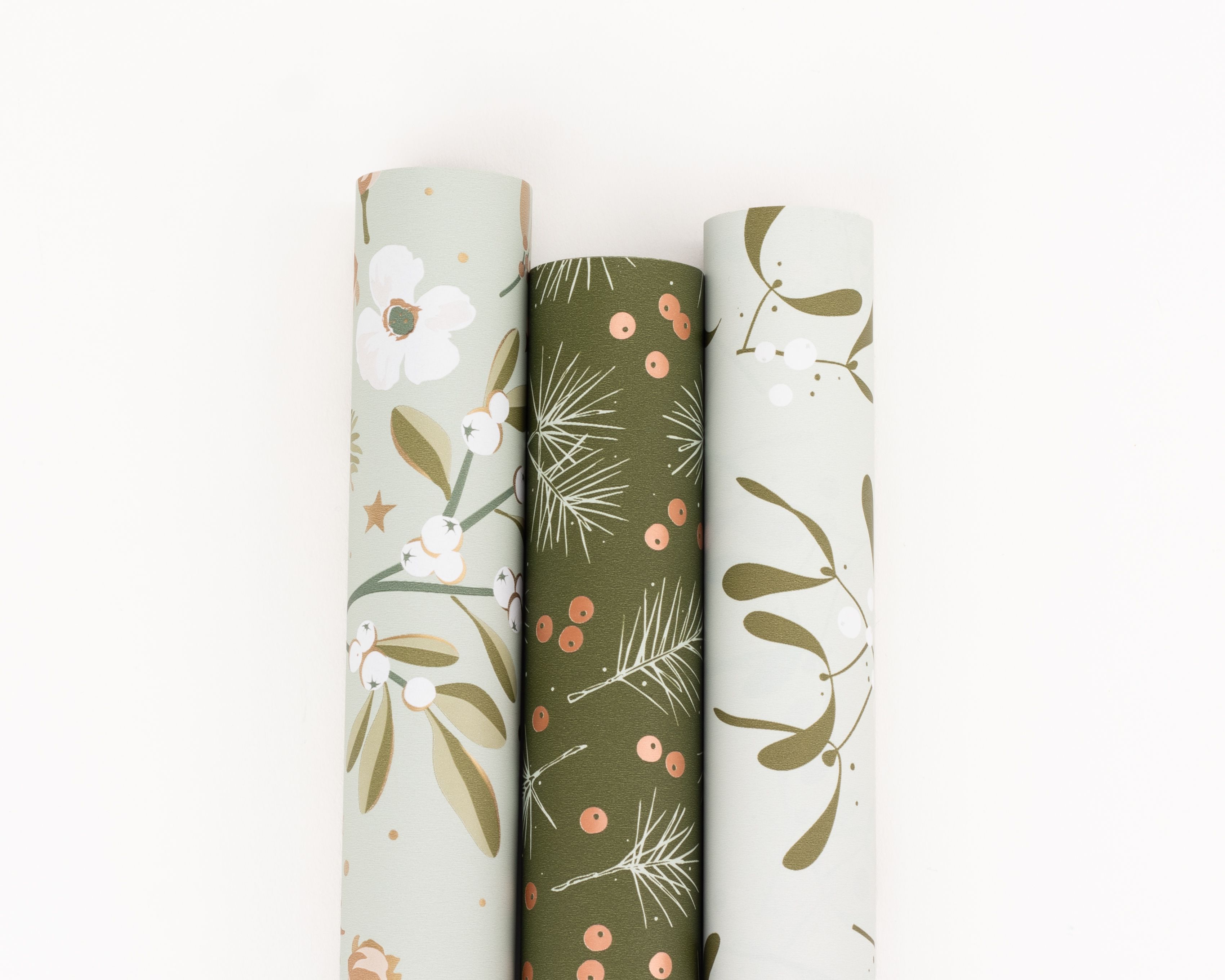 Geschenkpapier-Set mit drei Rollen in verschiedenen Grüntönen. Die Muster zeigen botanische Motive wie Blumen, Blätter, Beeren, Tannen und Sterne