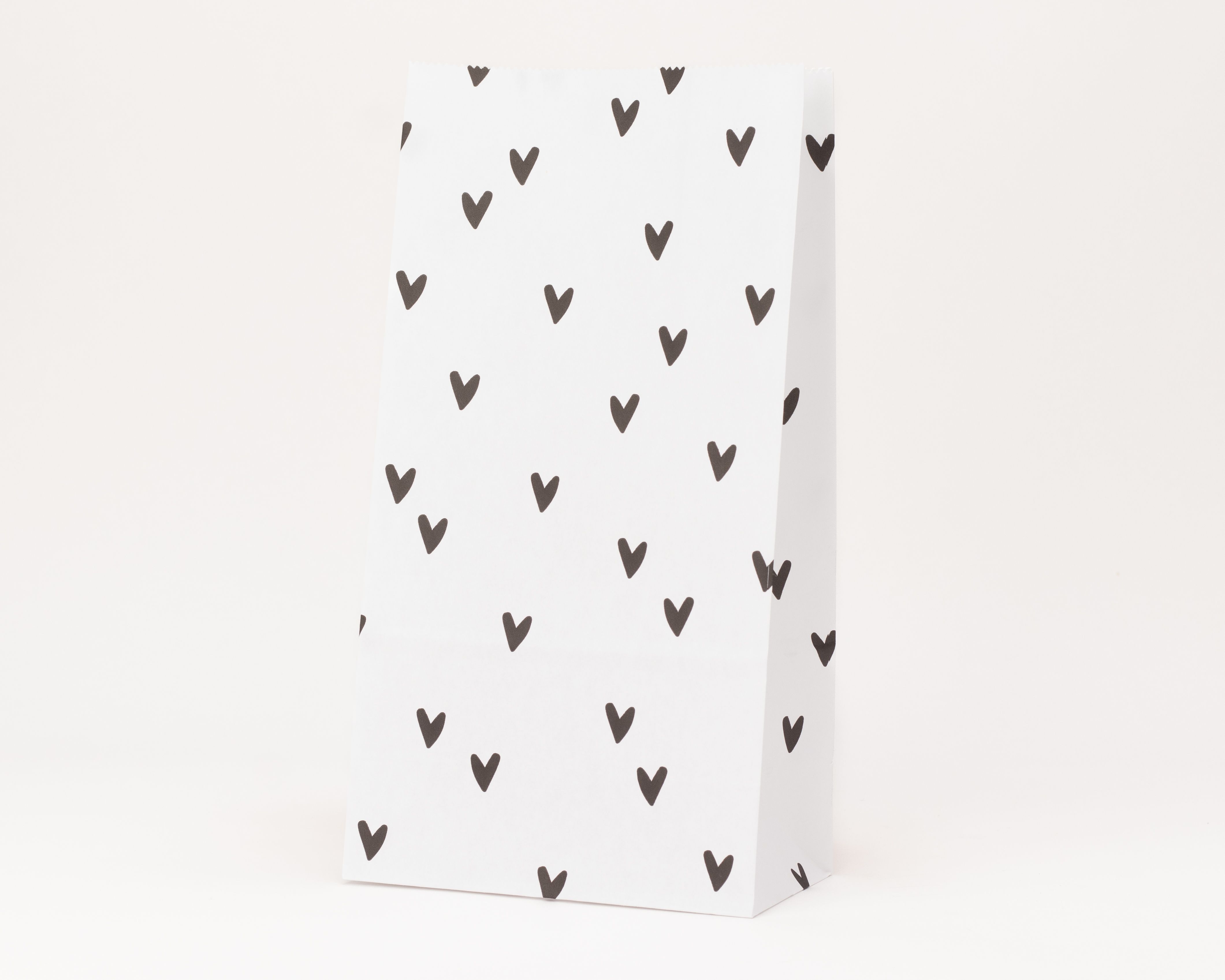 Papiertüten mit Blockboden, gefertigt aus weißem Papier und bedruckt mit einem Muster aus schwarzen Herzen