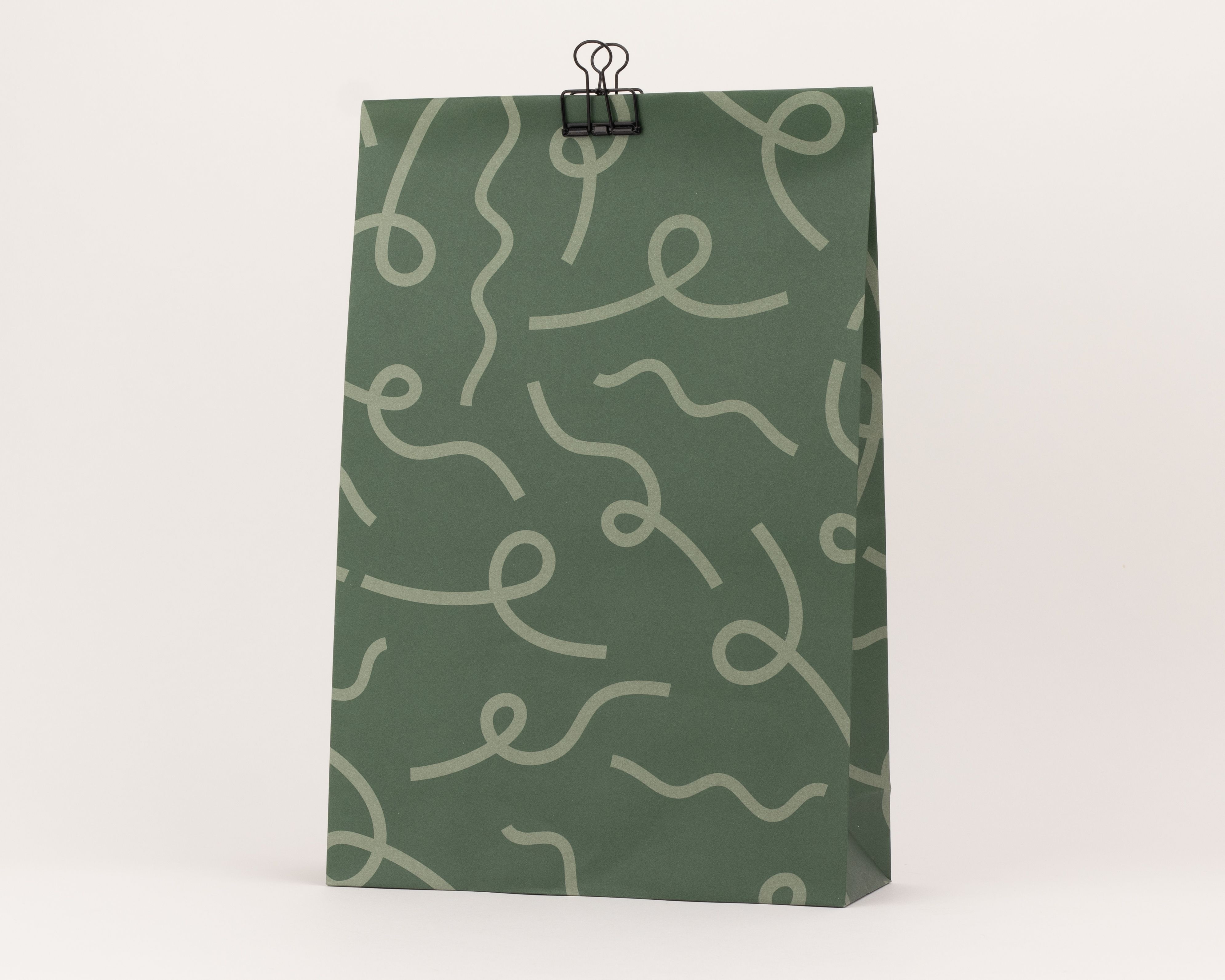 Blockbodenbeutel aus Papier in Dunkelgrün mit einem hellgrünen, wellenförmigen Schleifenmuster auf der Vorderseite
