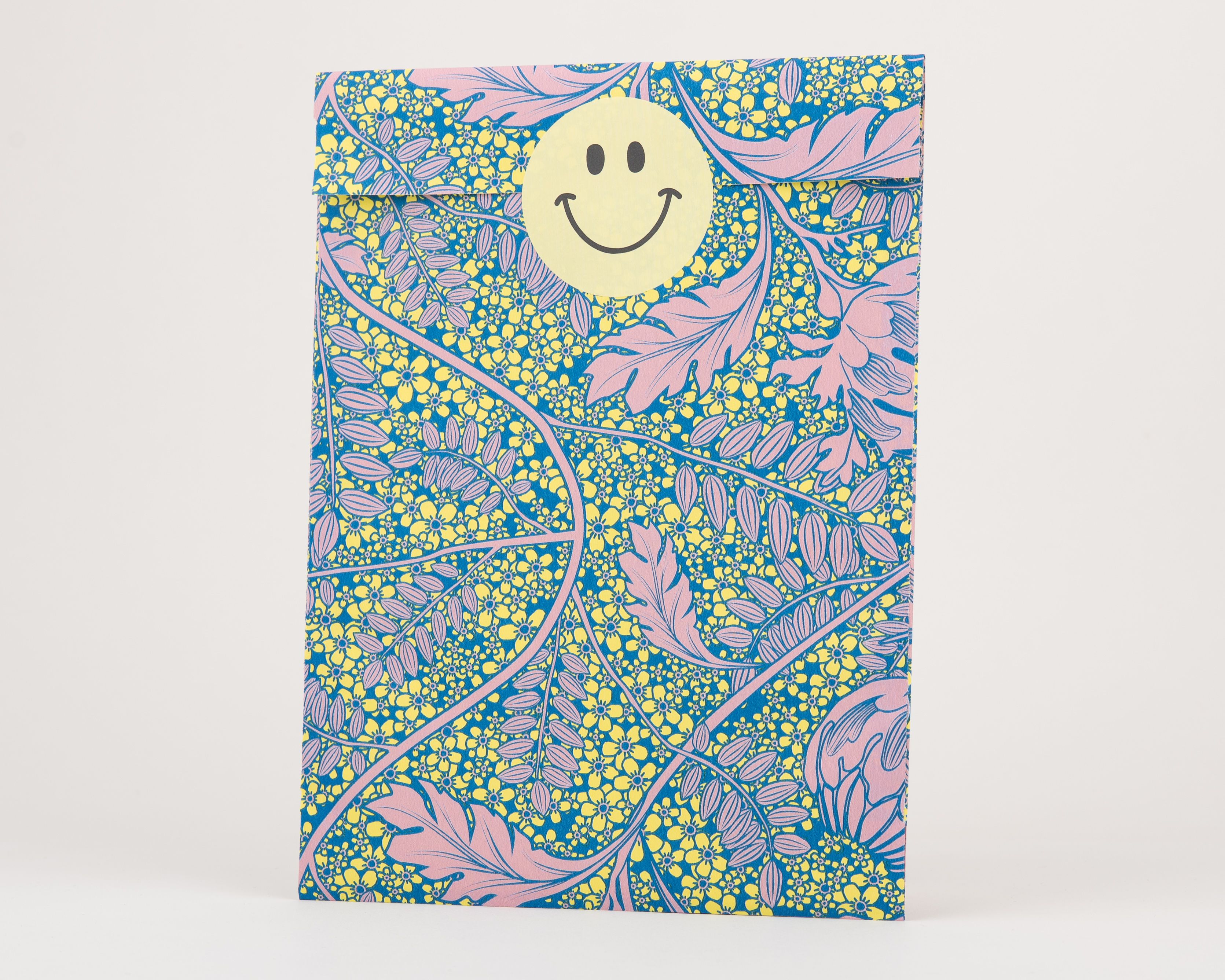 Papiertüten Flachbeutel mit einem Blumenmuster in Rosa, Blau und Gelb, ergänzt durch einen gelben Smiley-Aufkleber