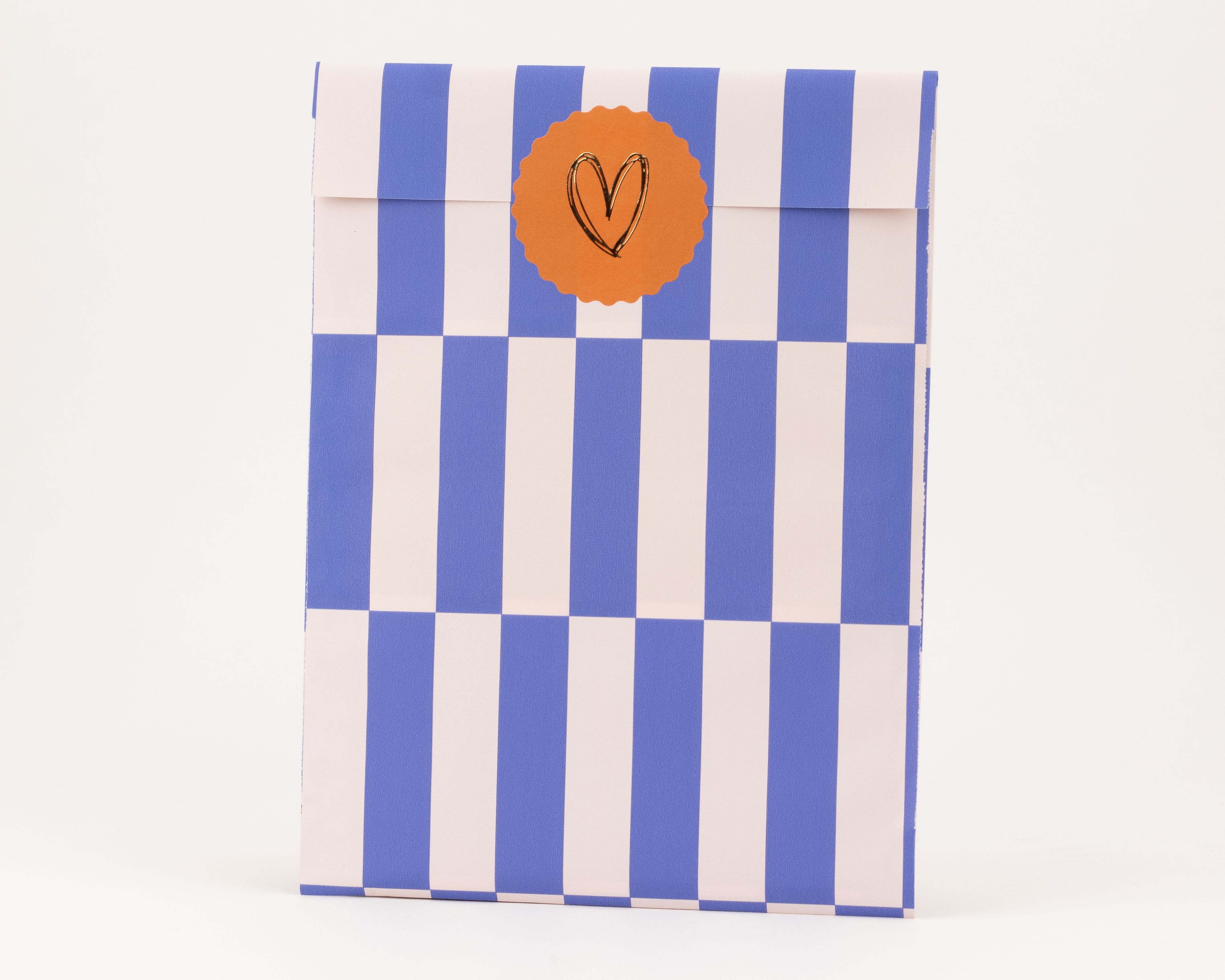 Flachbeutel mit blauen und elfenbeinfarbenen vertikalen Streifen. Ockerfarbener runder Sticker mit goldenem Herz. Innenseite ist Elfenbein