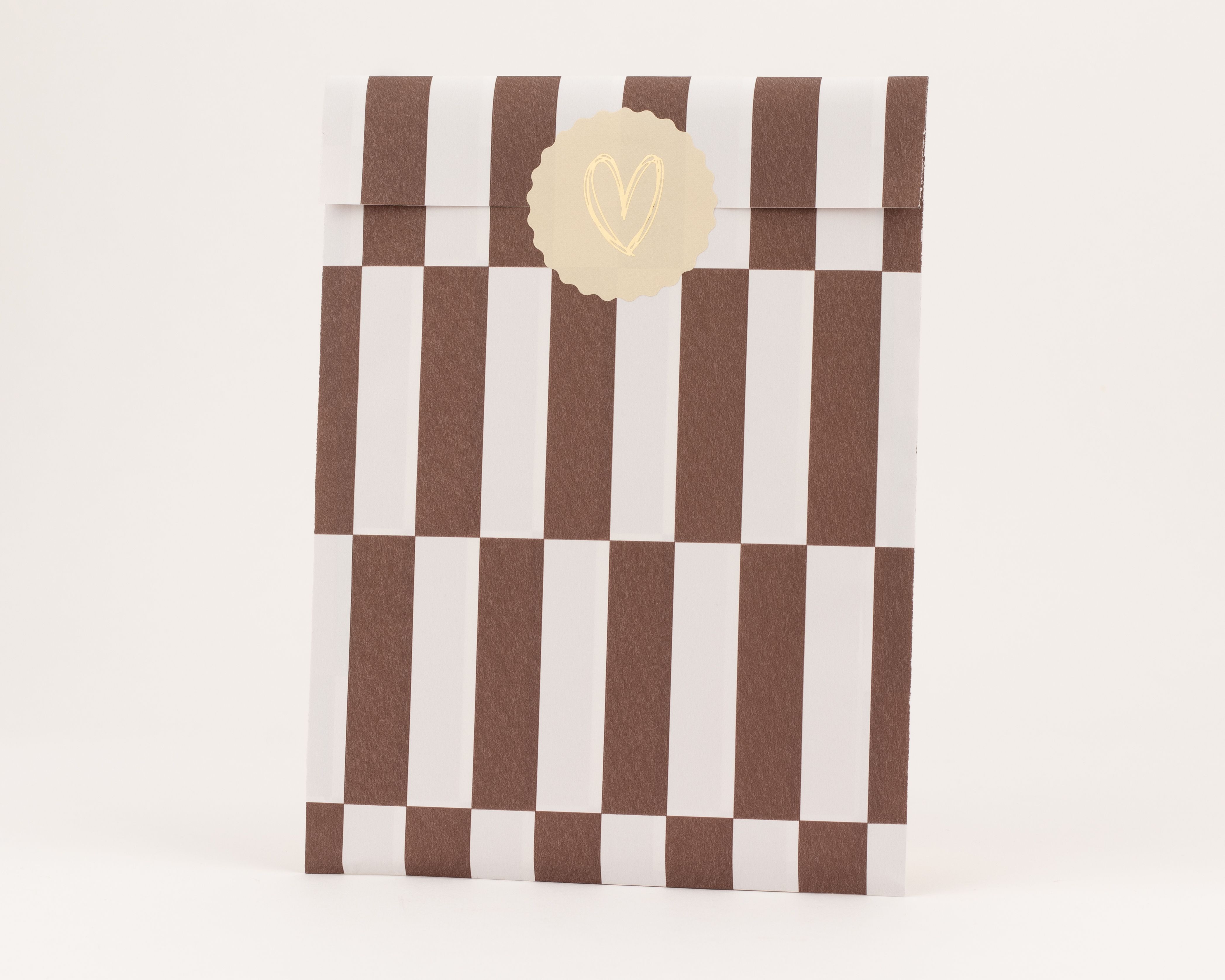 Flachbeutel mit markanten braun-weißen Streifen auf der Außenseite. Die Innenseite ist einheitlich weiß. Ein runder Aufkleber mit goldenem Herzmotiv ist sichtbar.