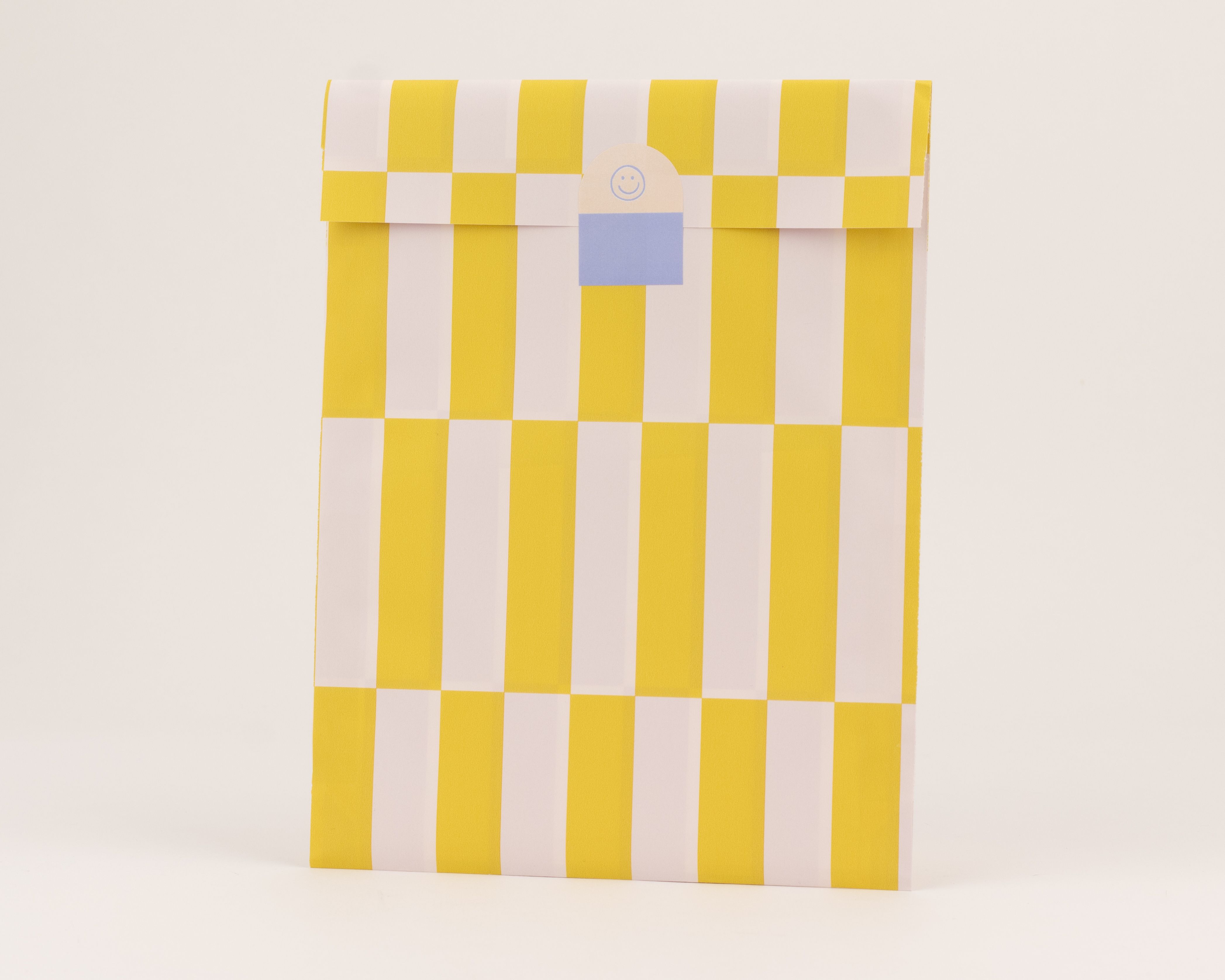 Flachbeutel mit auffälligen vertikalen Streifen in Gelb und Flieder auf der Außenseite, die Innenseite zeigt ein Karomuster in denselben Farben
