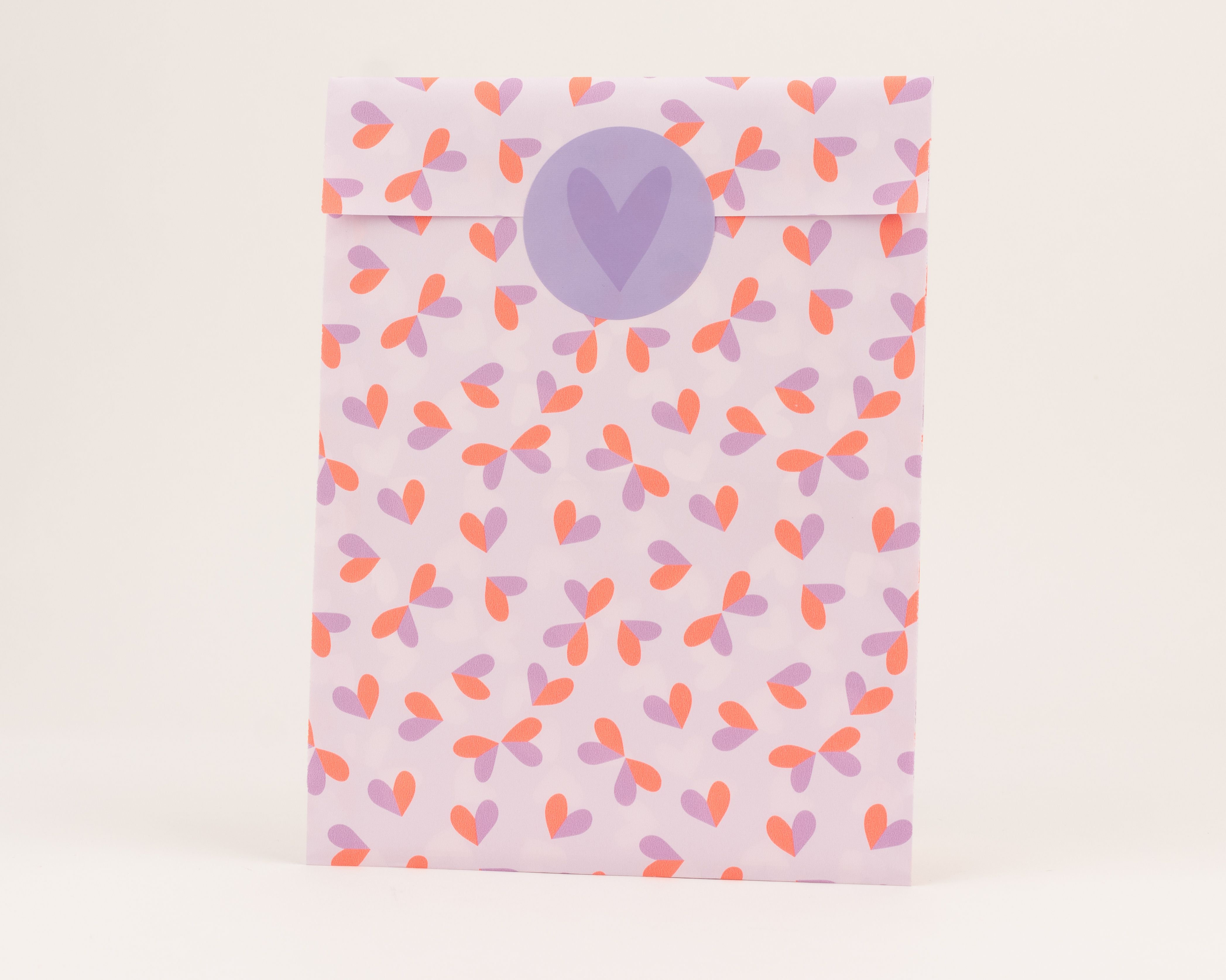 Flachbeutel mit durchgehendem Herzmuster in Hellflieder und Neon Orange. Die Innenseite ist Hellflieder und hat einen runden Aufkleber mit einem Herz.