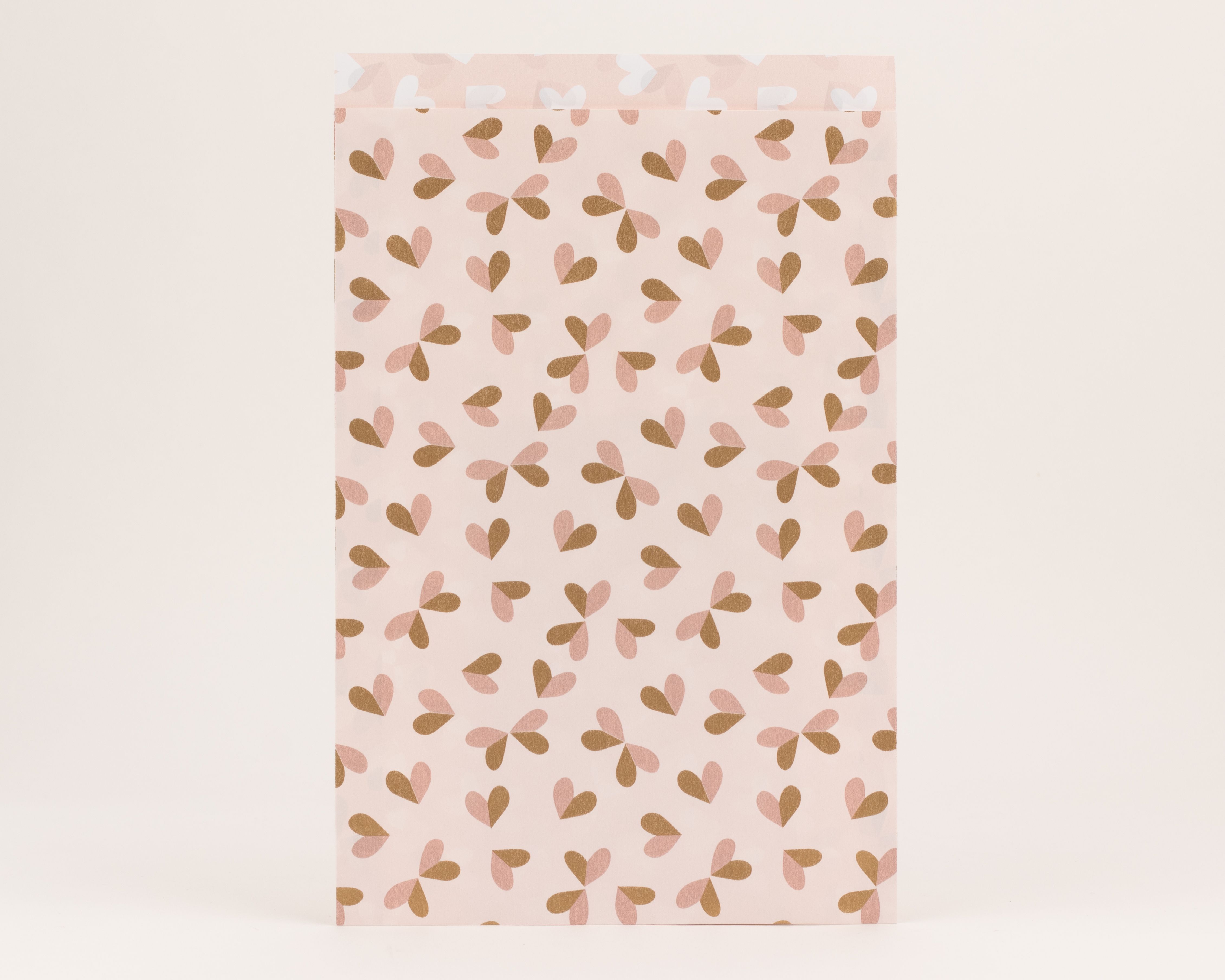 Flachbeutel mit einem Muster aus hellrosa und rostbraunen Herzen auf hellrosa Hintergrund, die Innenseite ist beige