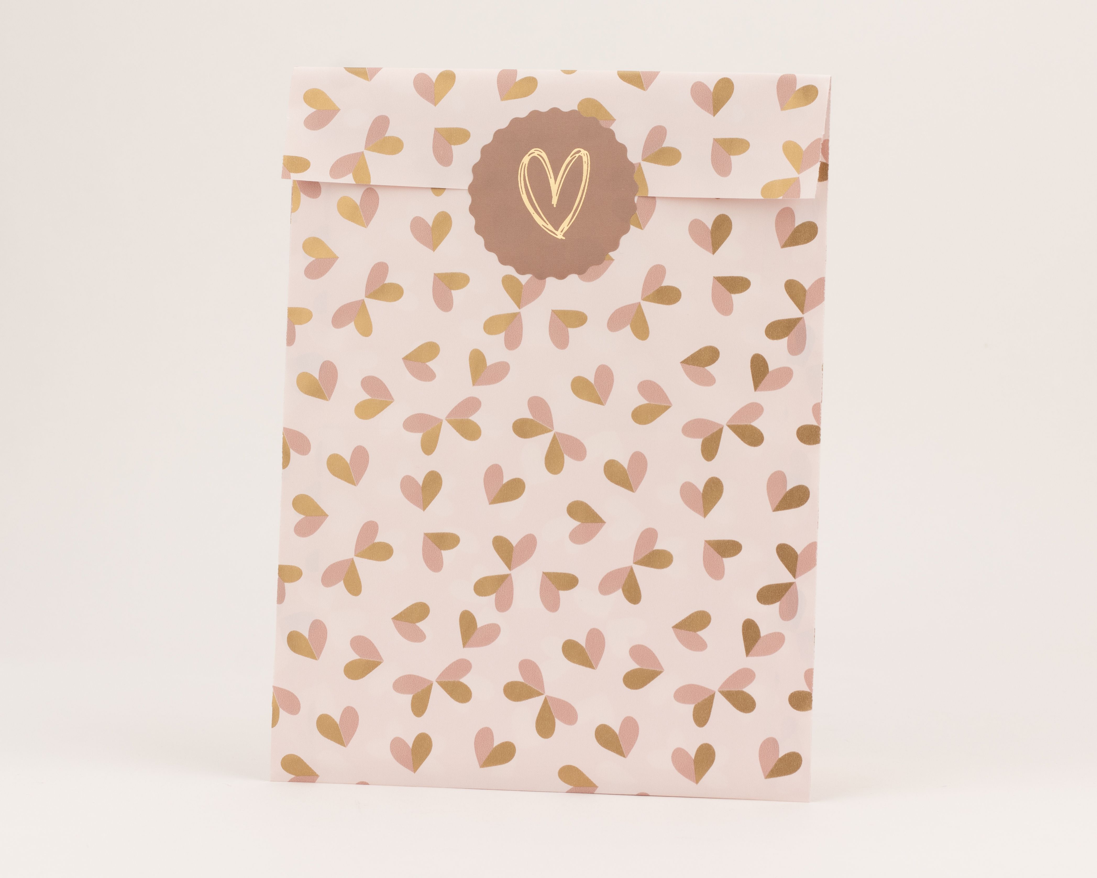 Flachbeutel mit Hellrosa- und Rostbraun-Herzmuster auf hellrosafarbenem Grund. Ein rostbrauner runder Aufkleber mit goldenem Herz