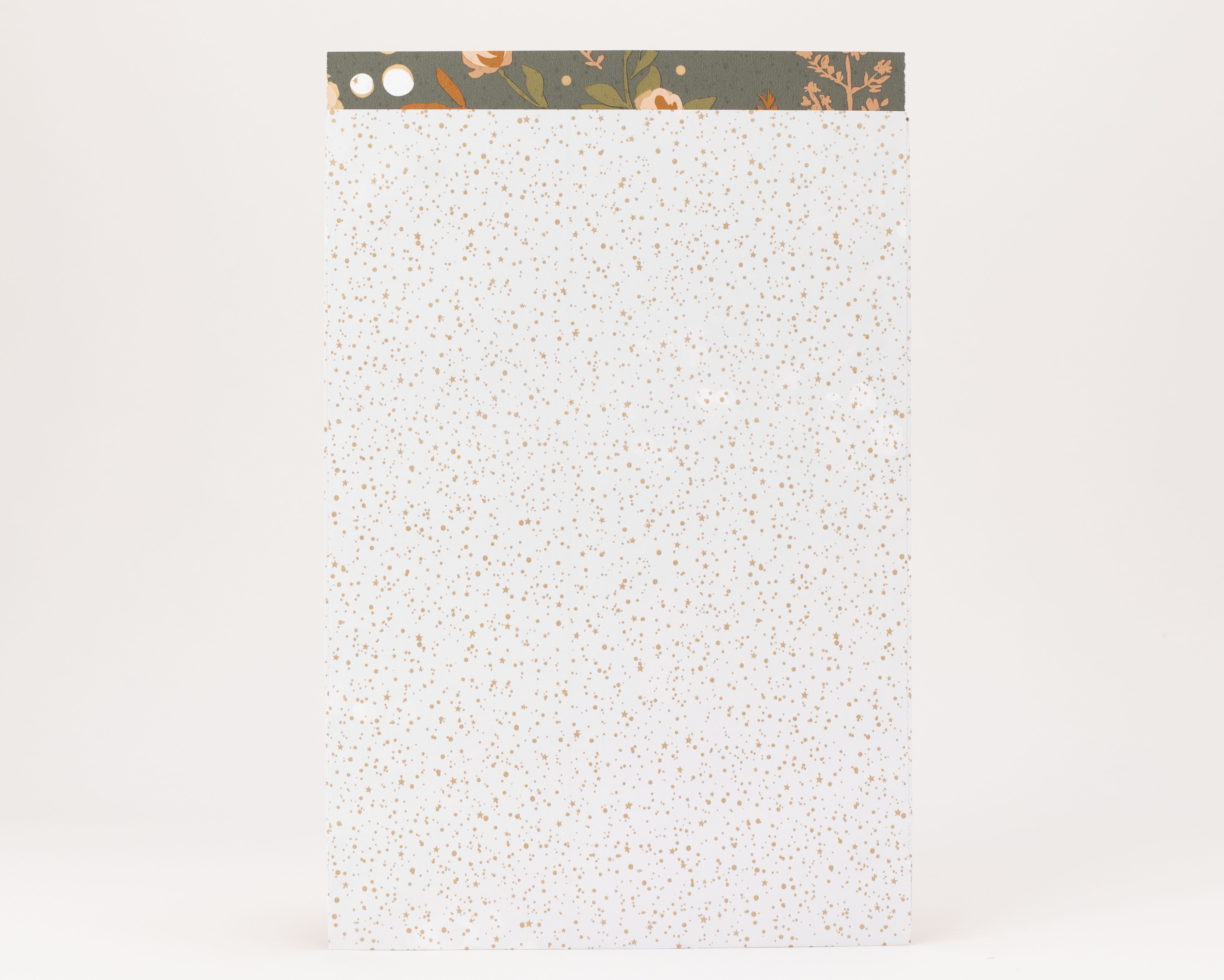 Flachbeutel in Weiß mit funkelnden goldenen Sternen und Punkten, die Innenseite hat ein florales Muster mit orangefarbenen Blüten auf olivgrünem Grund