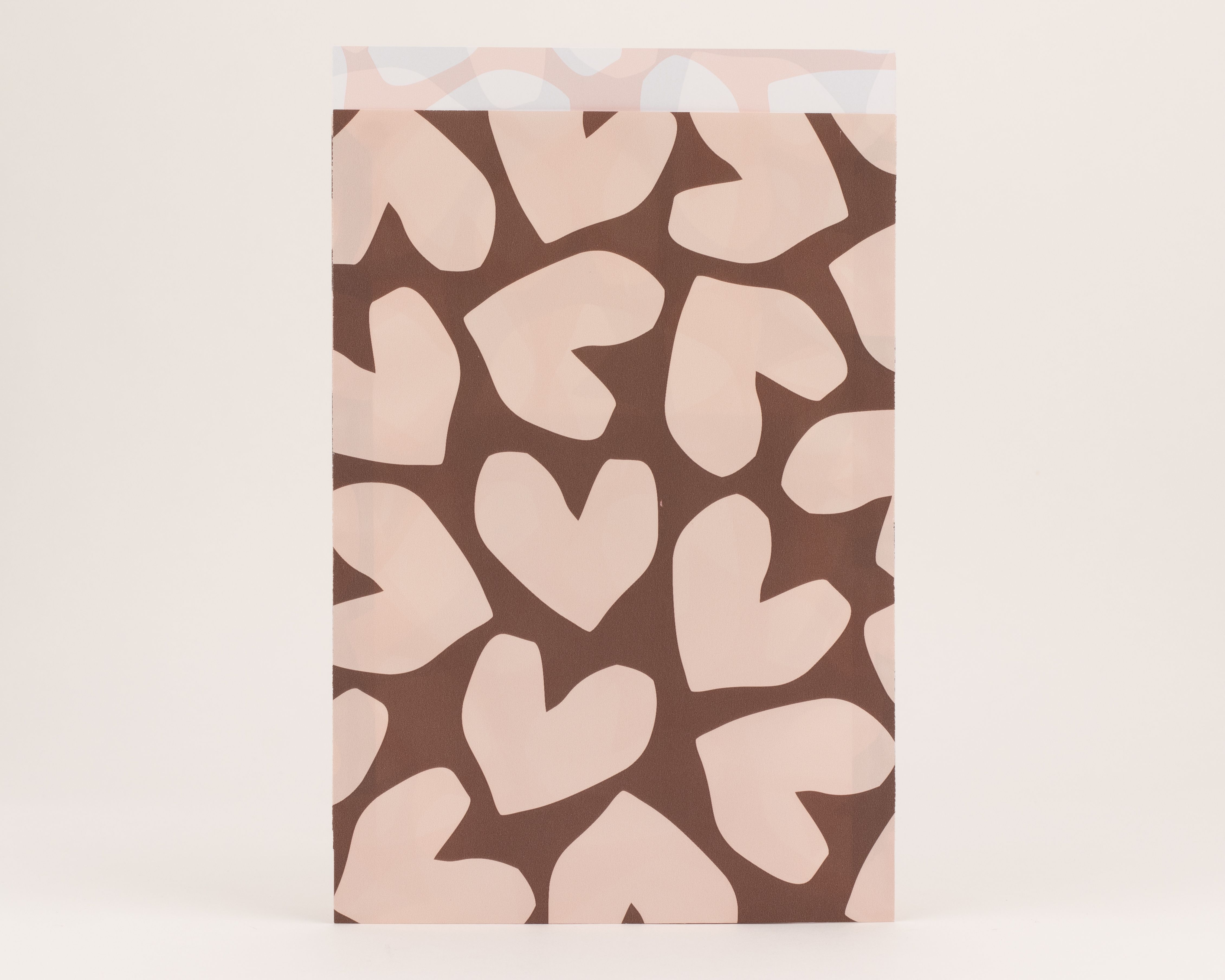 Flachbeutel mit brauner Außenseite und beigem Herzmuster. Die helle Innenseite zeigt eine zarte, beige Musterung.