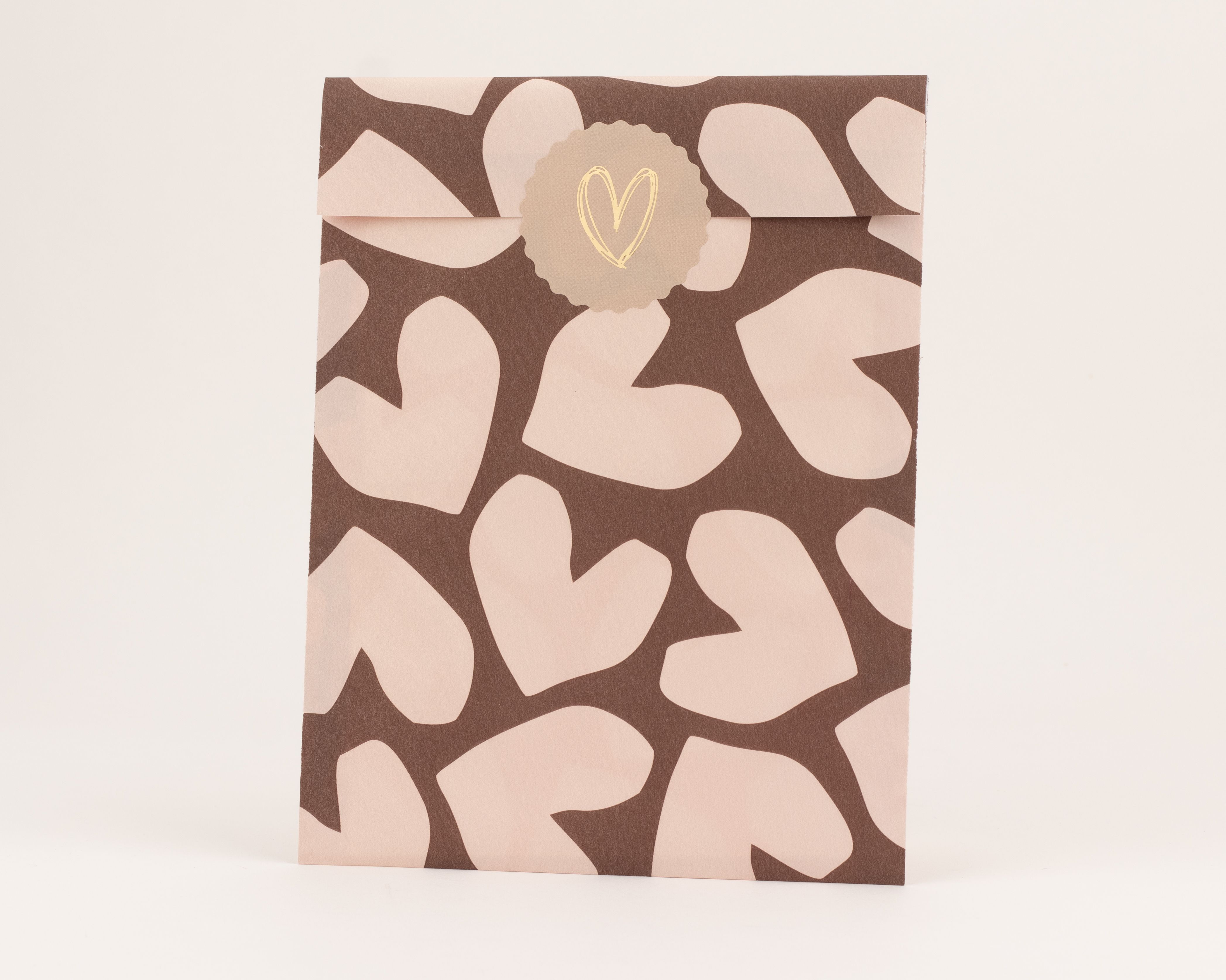 Flachbeutel in Braun mit beigen Herzmustern. Die Innenseite ist Beige, verziert mit einem runden Aufkleber und goldenem Herzmotiv