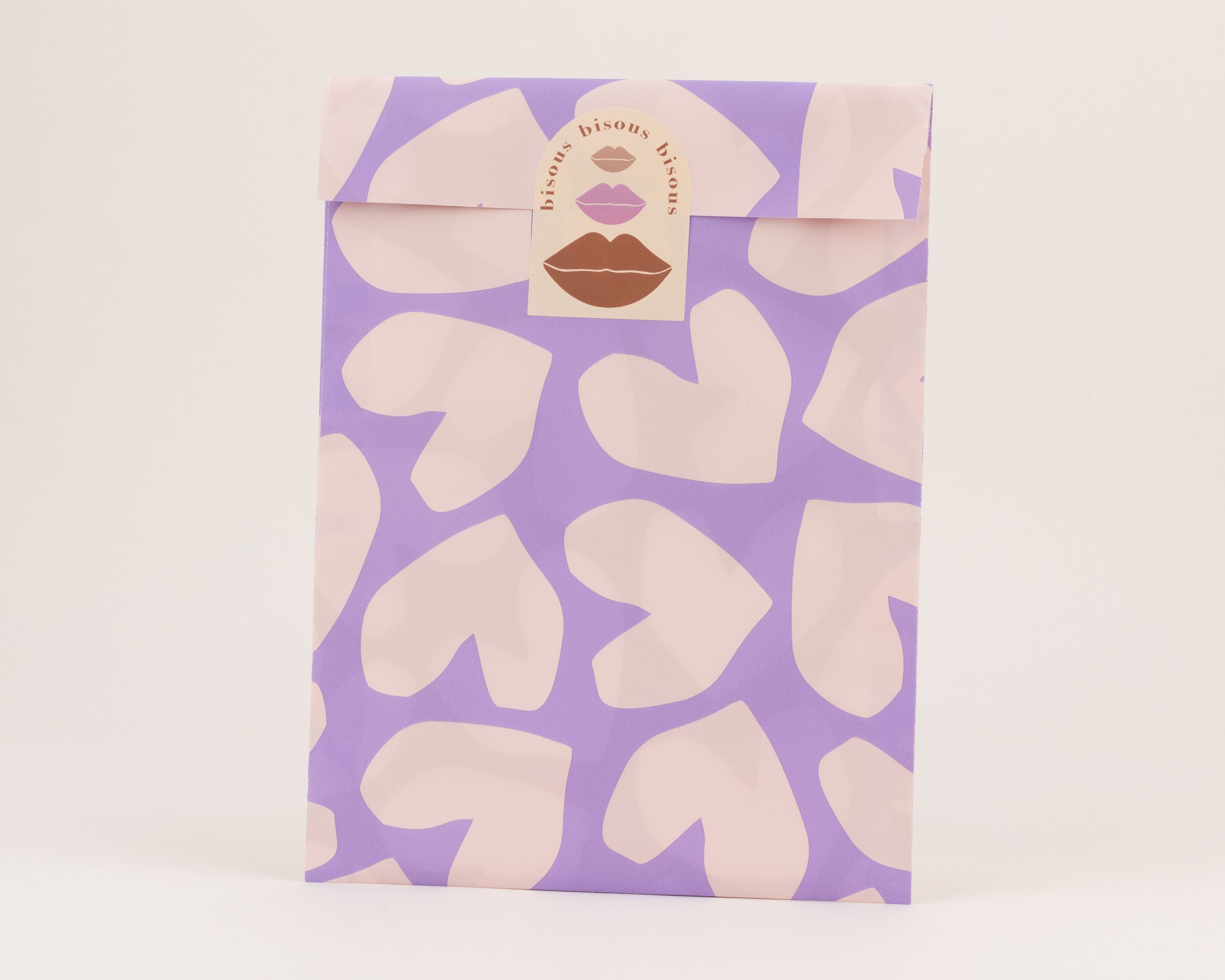 Flachbeutel mit hellfliederfarbenen Herzen auf lilafarbenem Grund, akzentuiert durch einen Aufkleber mit Lippen in Rost.