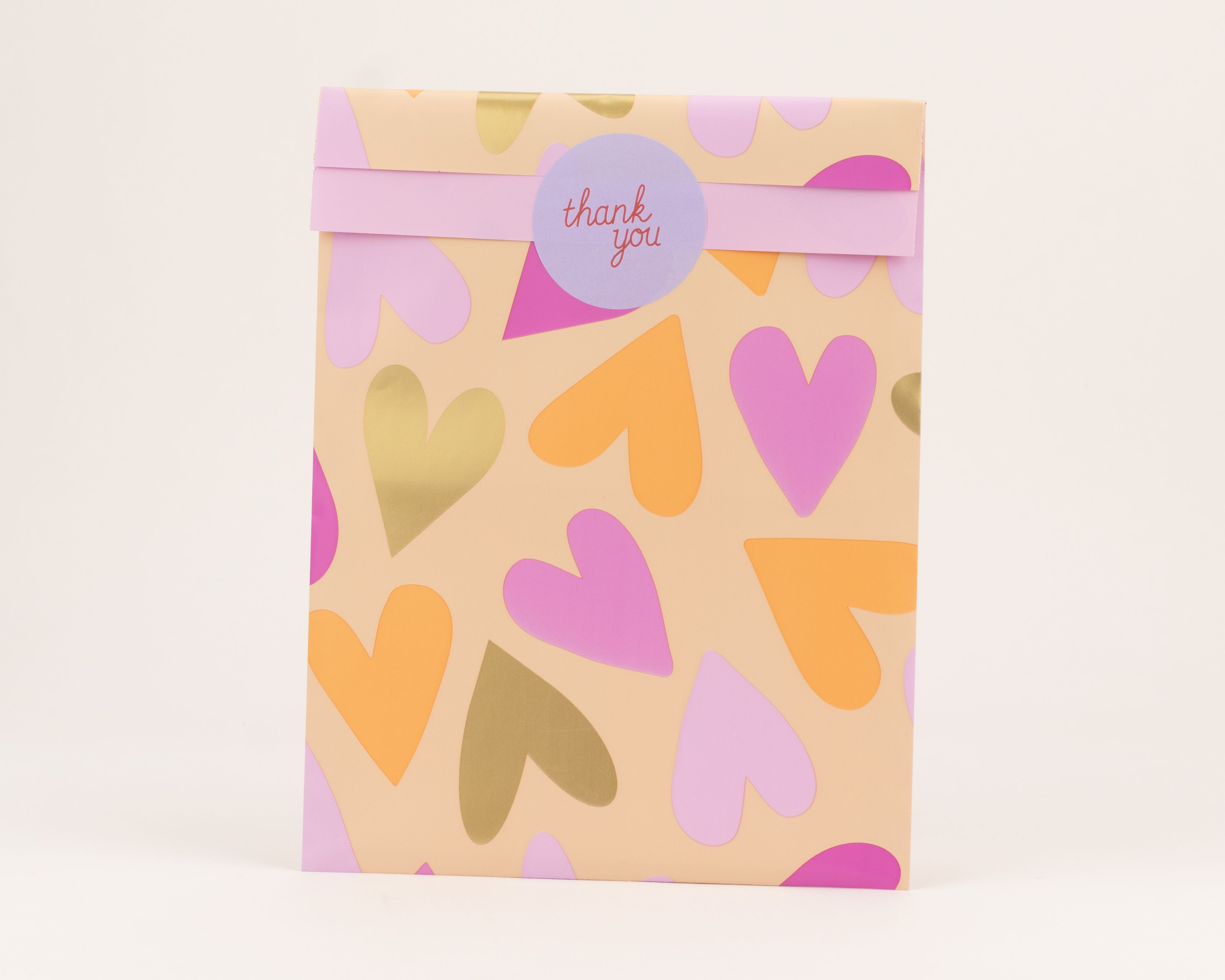 Flachbeutel mit pinken, orangenen und goldenen Herzen auf pfirsichfarbenem Grund. Ein pinkes Band mit 'Thank you' Aufkleber ist sichtbar, die Innenseite ist pfirsichfarben