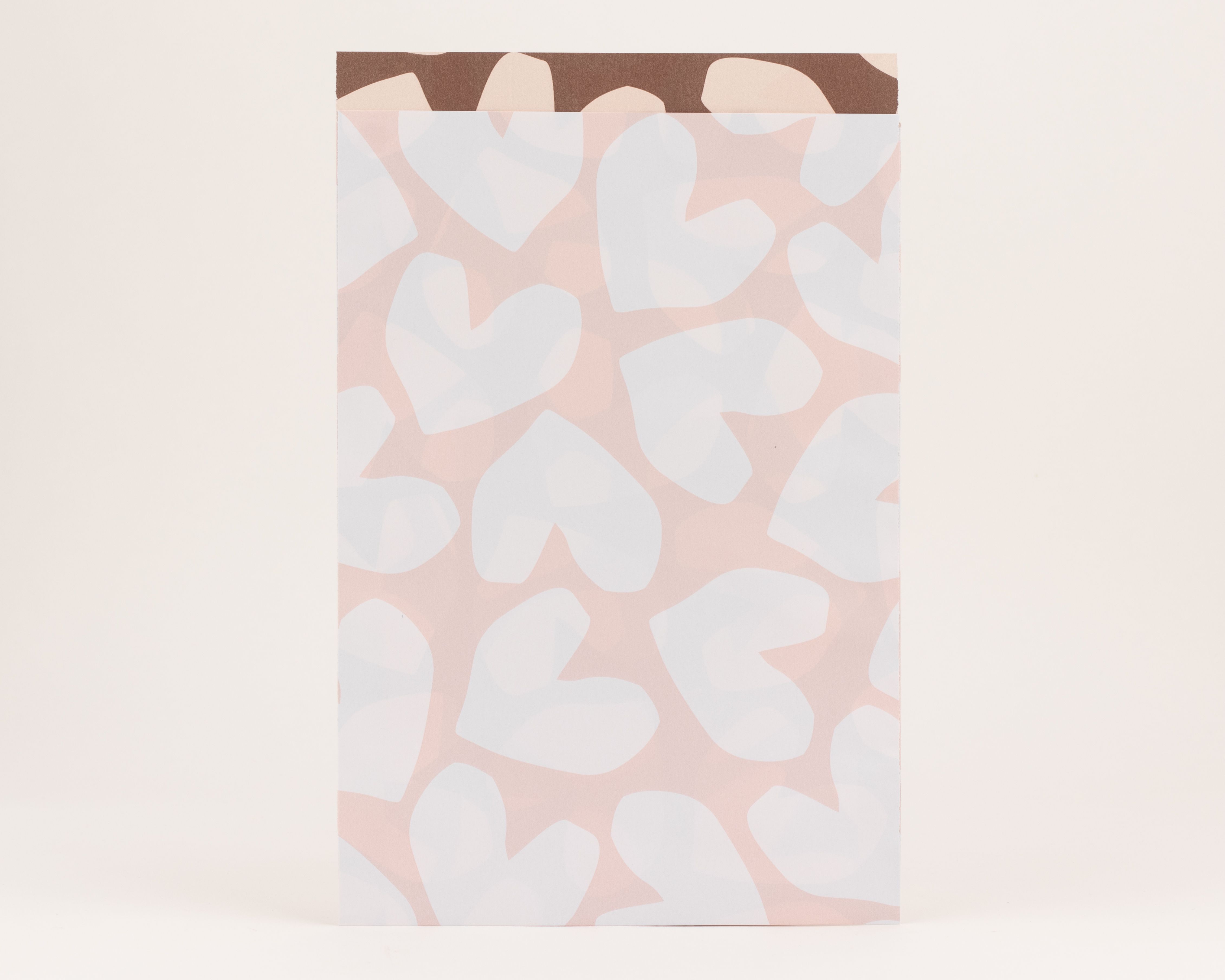 Flachbeutel mit rosa Außenseite und weißem Herzmuster, die Innenseite ist mit einem braun-beigen abstrakten Muster gestaltet