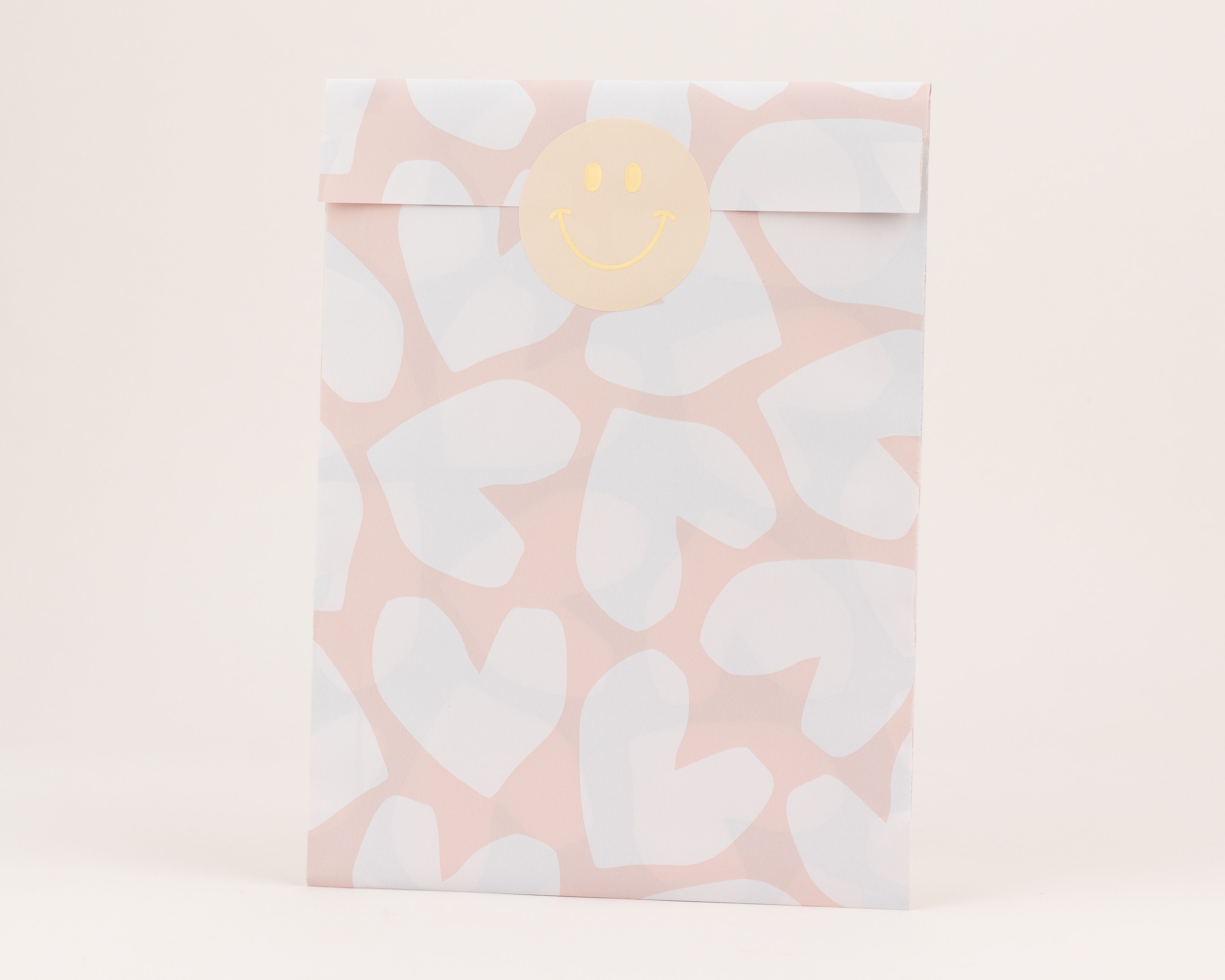 Flachbeutel mit rosafarbenem Hintergrund und weißen Herzen, die Innenseite ist weiß, darüber ein beiger Smiley-Aufkleber