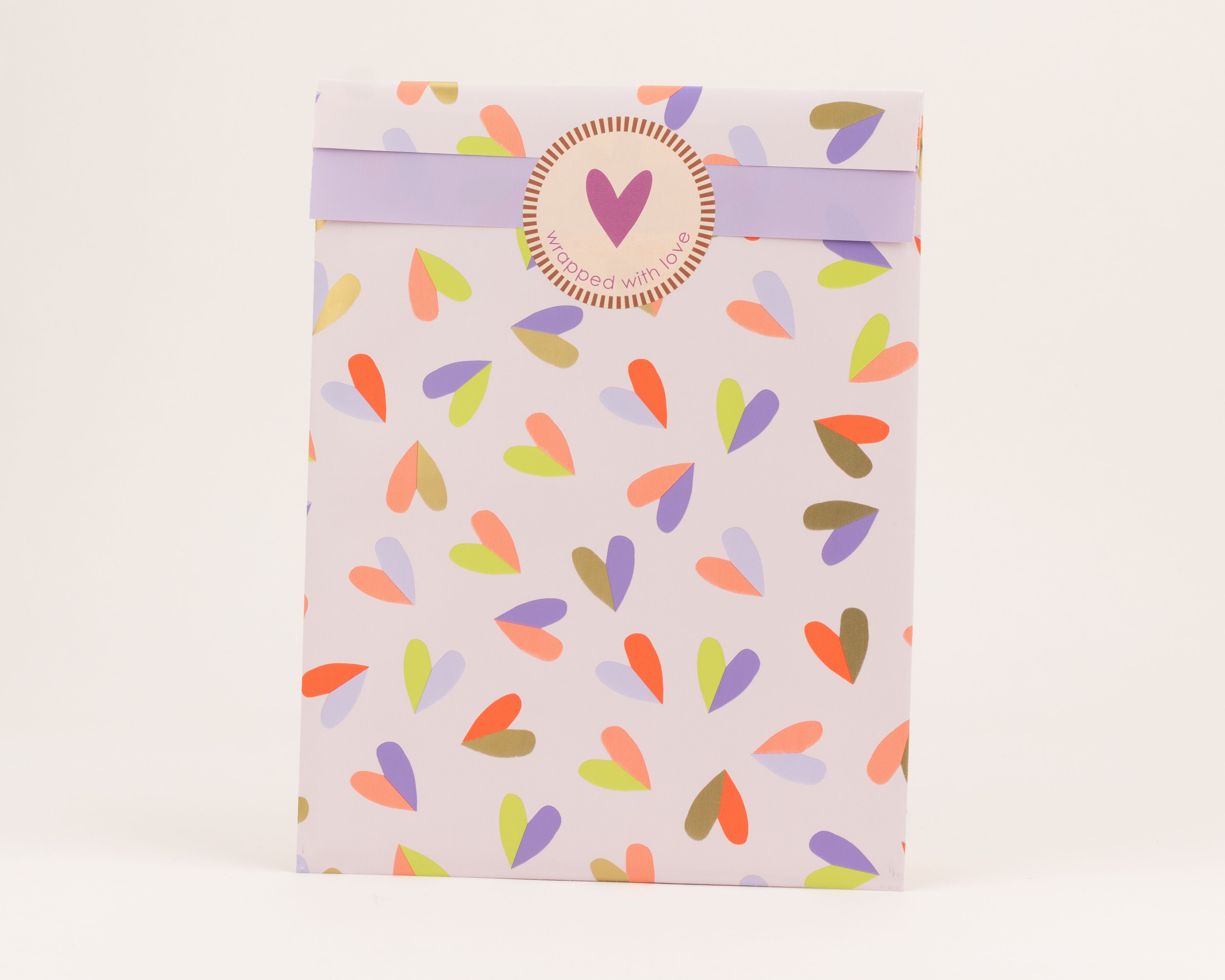 Flachbeutel mit einem Herzmuster in Orange, Violett und Limettengrün auf hellviolettem Grund. Die Innenseite ist fliederfarben