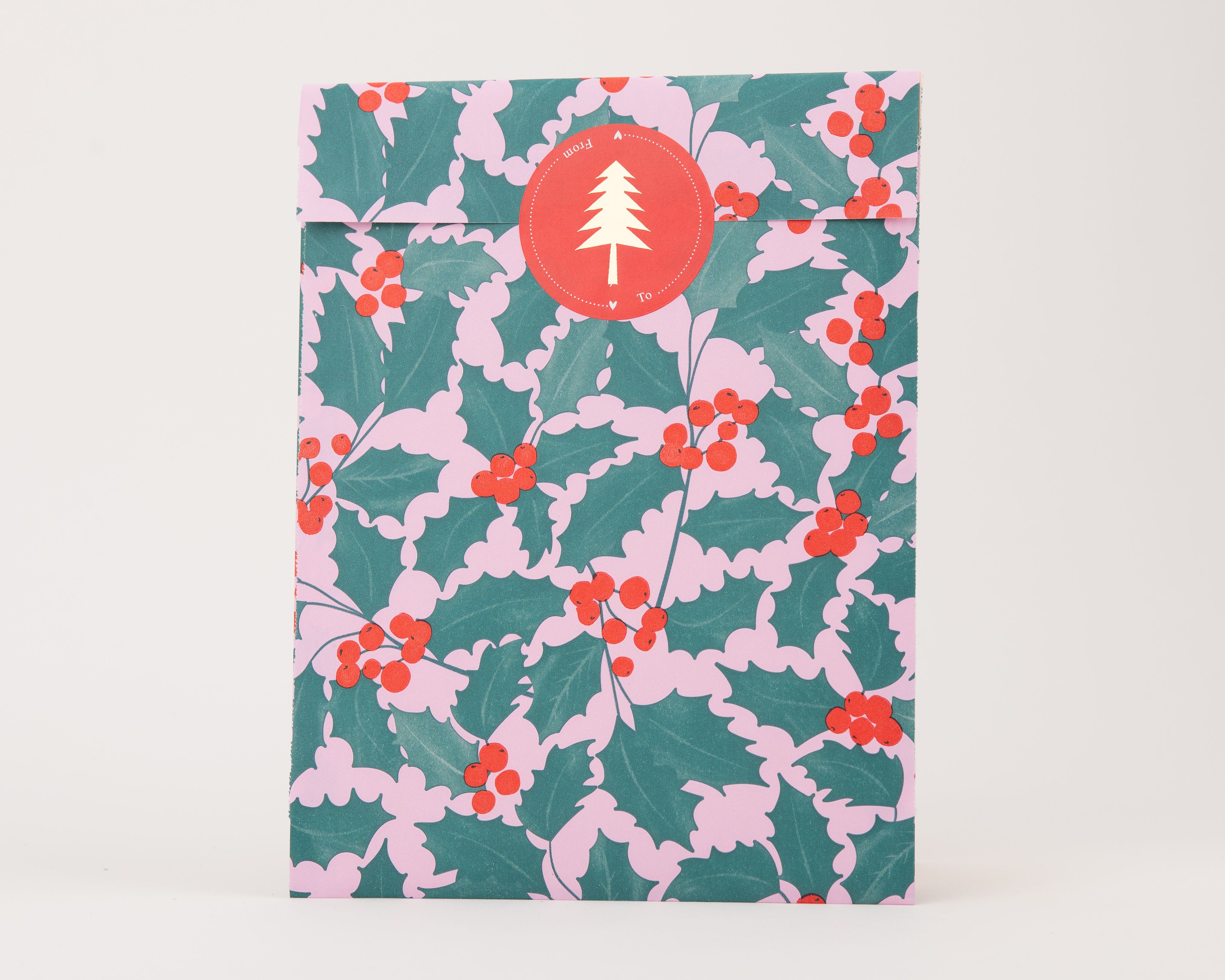 Papiertüten Flachbeutel mit Ilex-Muster aus grünen Blättern auf rosa Hintergrund, roten Beeren und beigem Weihnachtsbaum auf rotem Aufkleber