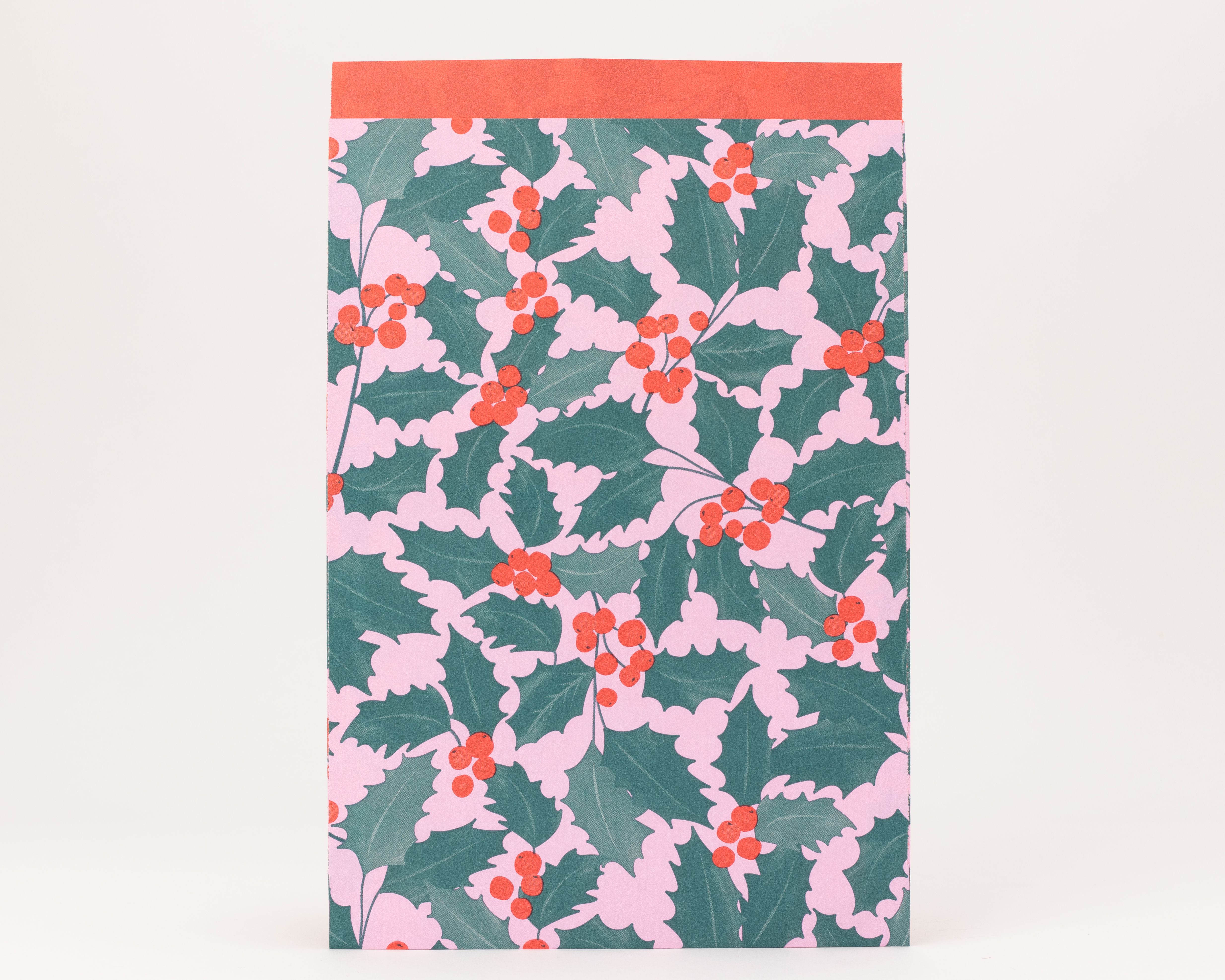 Flachbeutel mit Ilex-Muster in Rosa, Grün und Rot. Grüne Blätter und rote Beeren auf rosa Hintergrund, die Innenseite ist rot