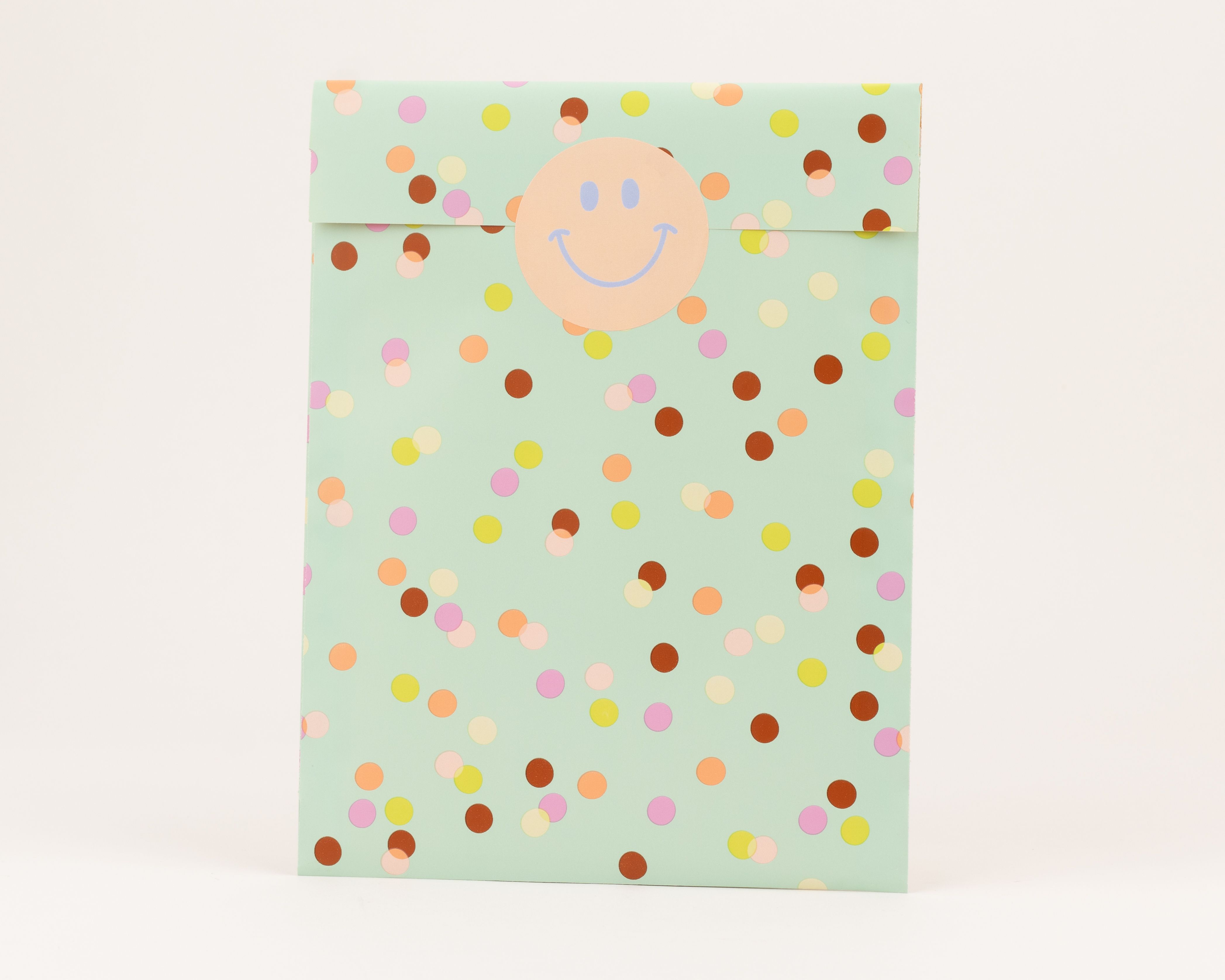 Flachbeutel in Minzgrün mit farbenfrohem Konfetti-Muster in Orange, Braun, Gelb und Pink, verschlossen mit einem runden Smiley-Aufkleber
