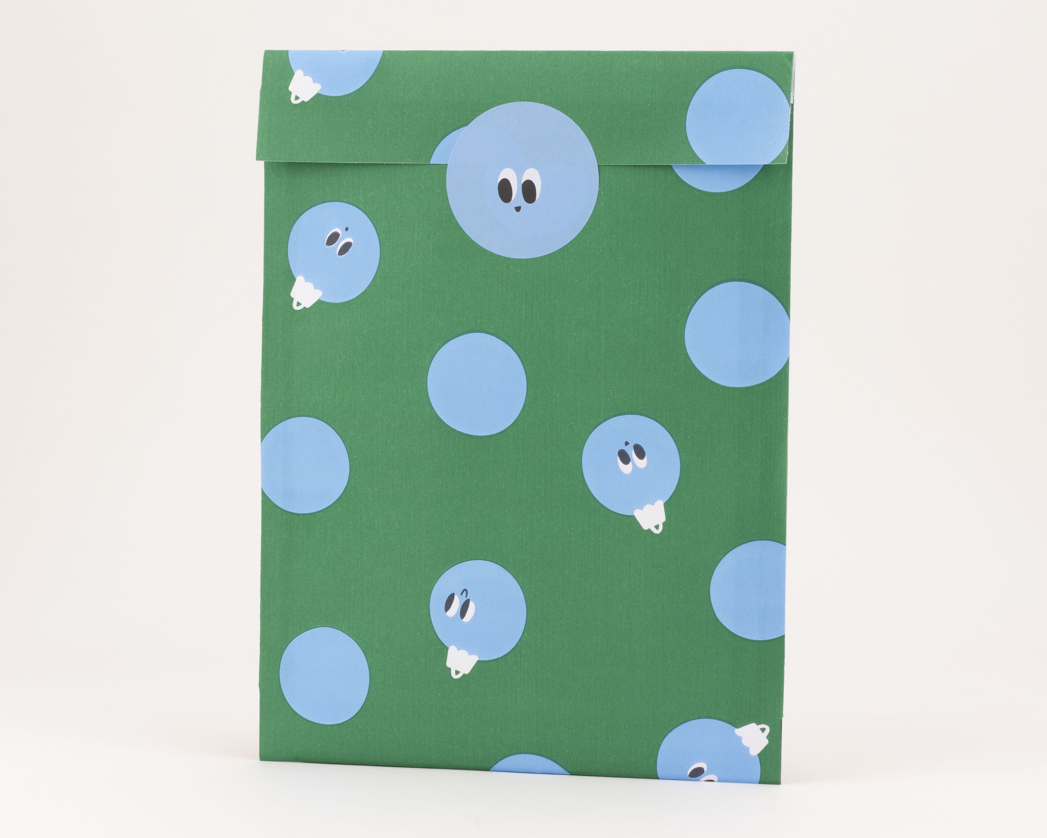 Papiertüten mit grünem Hintergrund und einem Muster aus blauen Kugeln, die teilweise Gesichter zeigen
