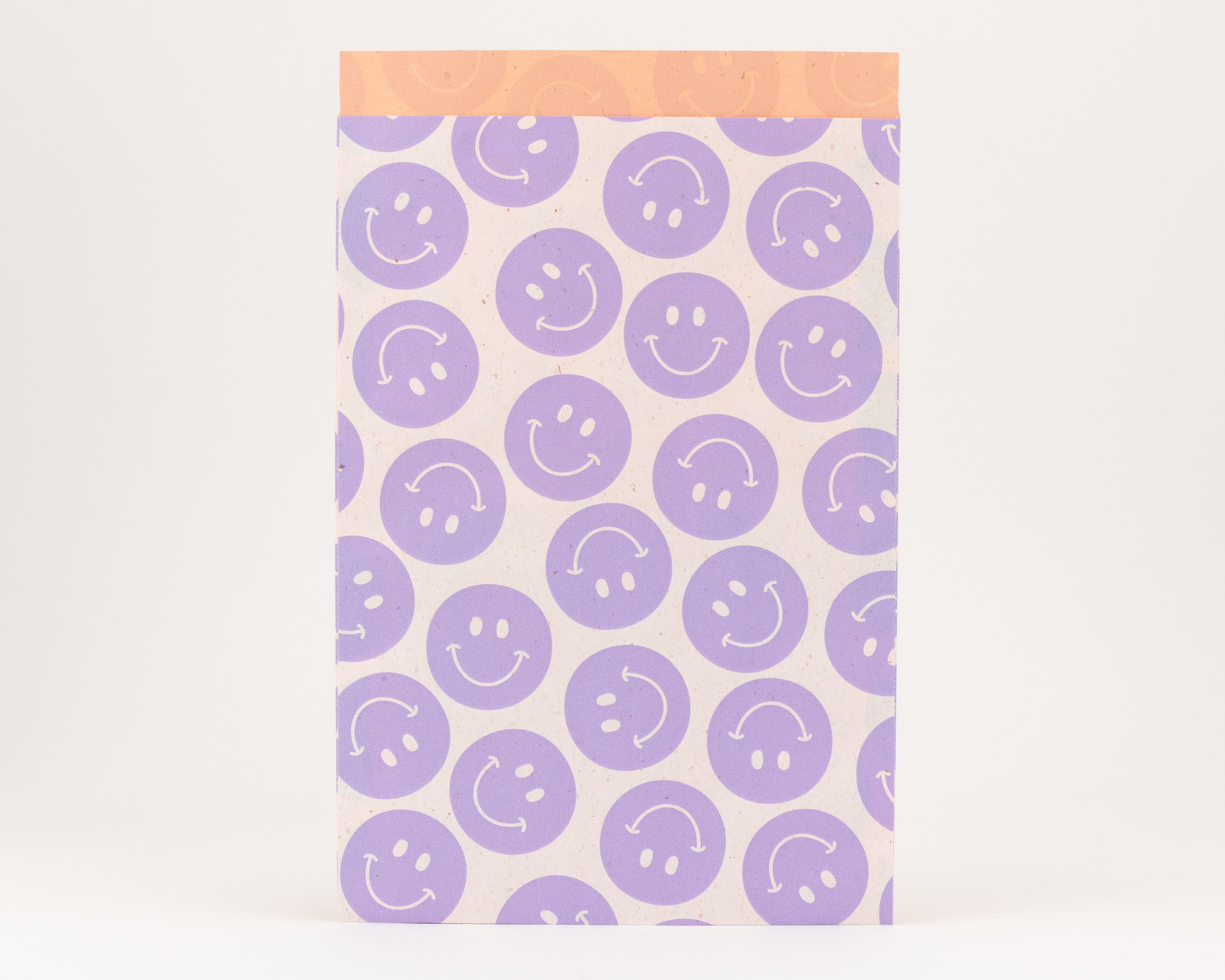 Flachbeutel mit fliederfarbenen Smileys auf der hellen Außenseite und einer orangefarbenen Innenseite mit dezentem Muster