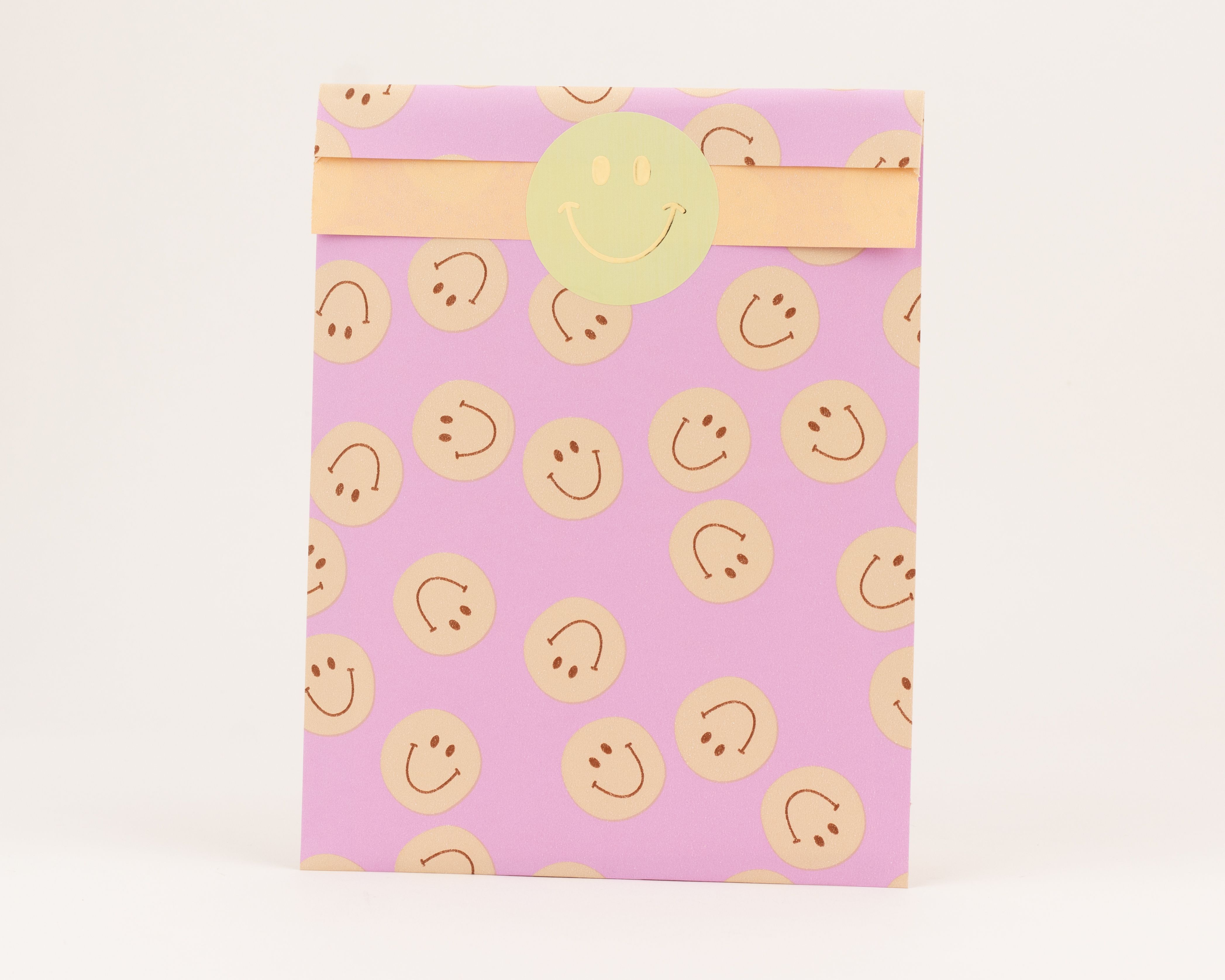 Flachbeutel mit fliederfarbener Außenseite, verziert mit beige Smileys; die Innenseite ist orangefarben.