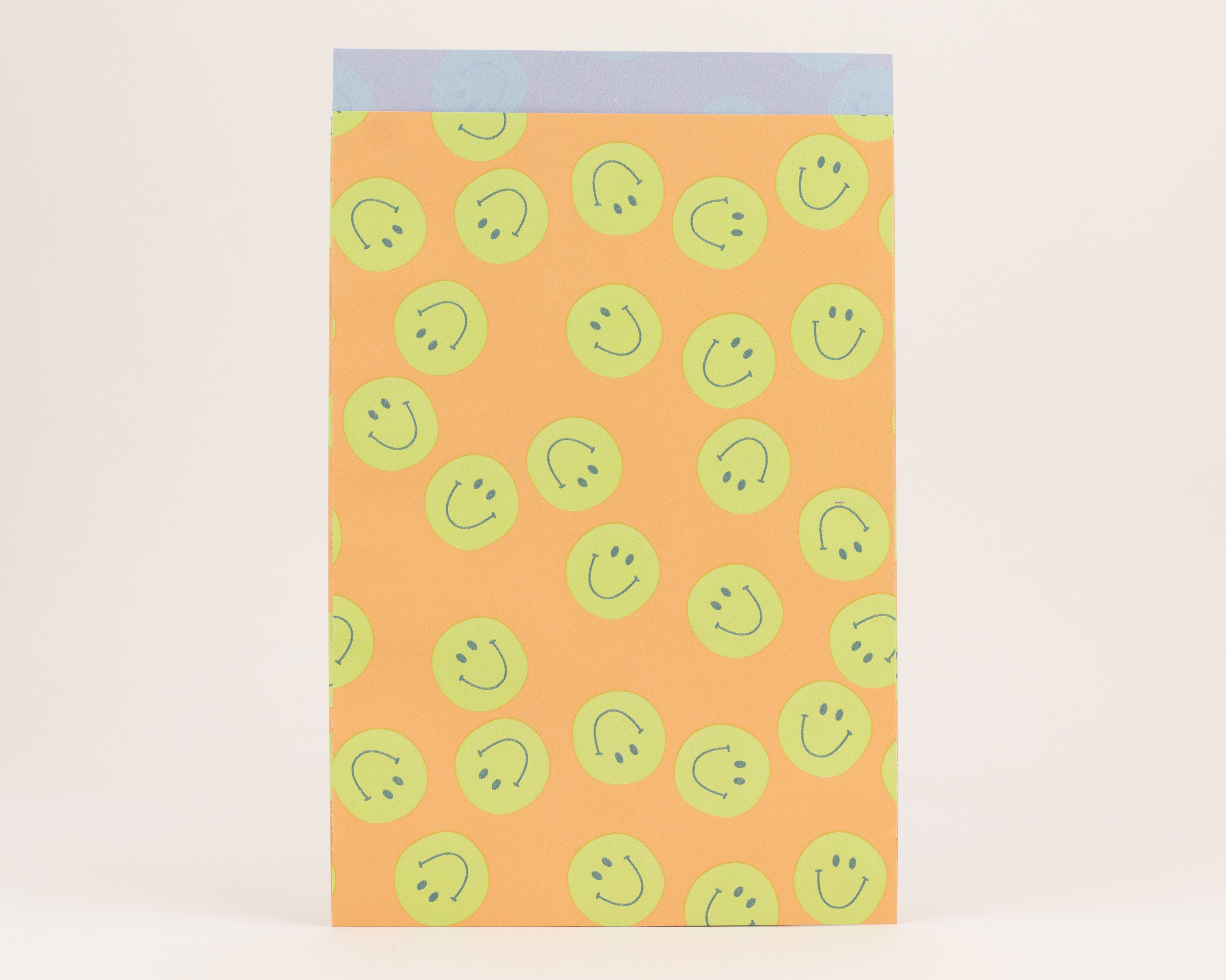Flachbeutel mit einem Muster aus grünen Smileys auf orangefarbener Außenseite und blauer Innenseite