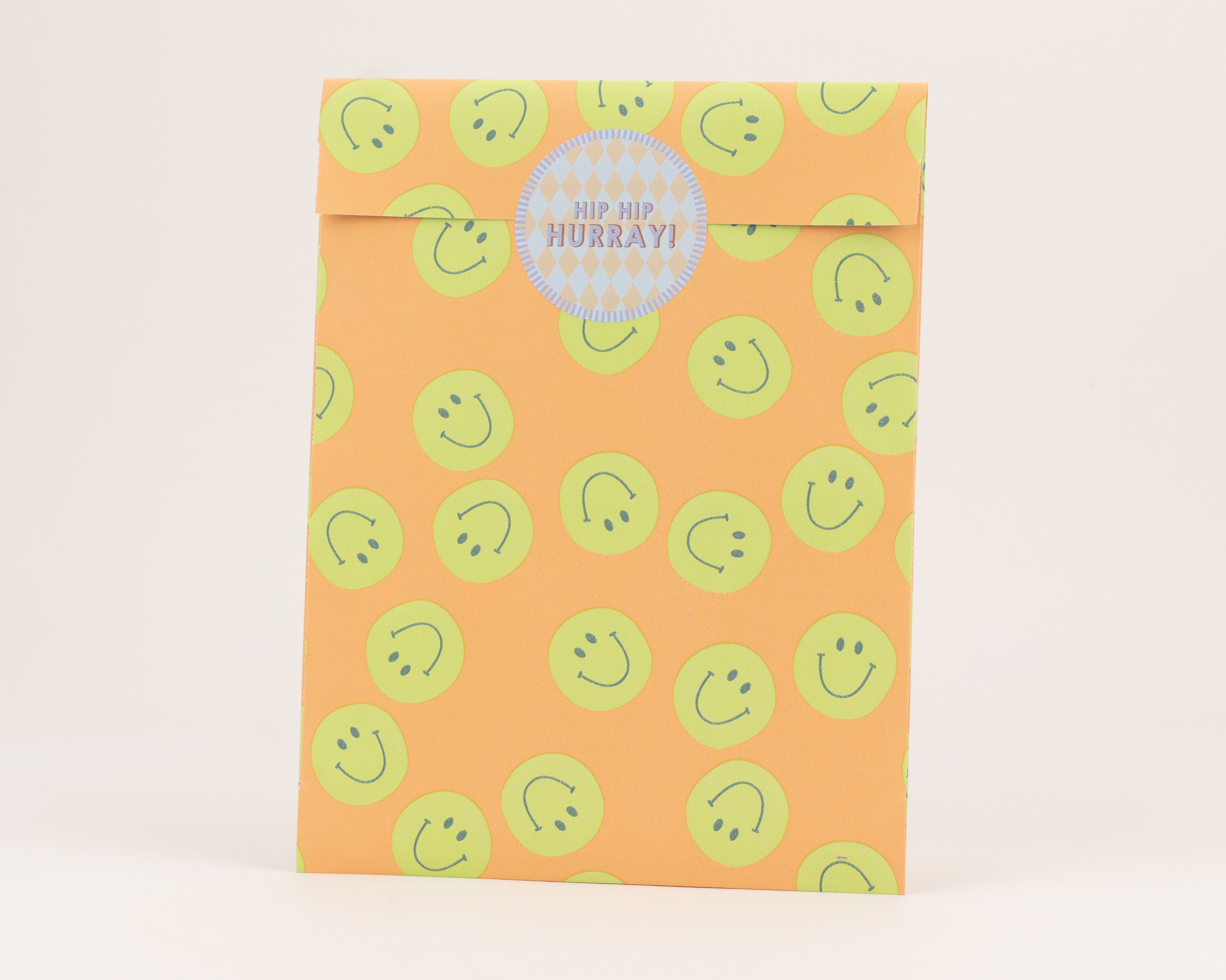 Flachbeutel in Orange mit gruenen Smileys auf der Außenseite und blauem Rautenmuster auf der Innenseite