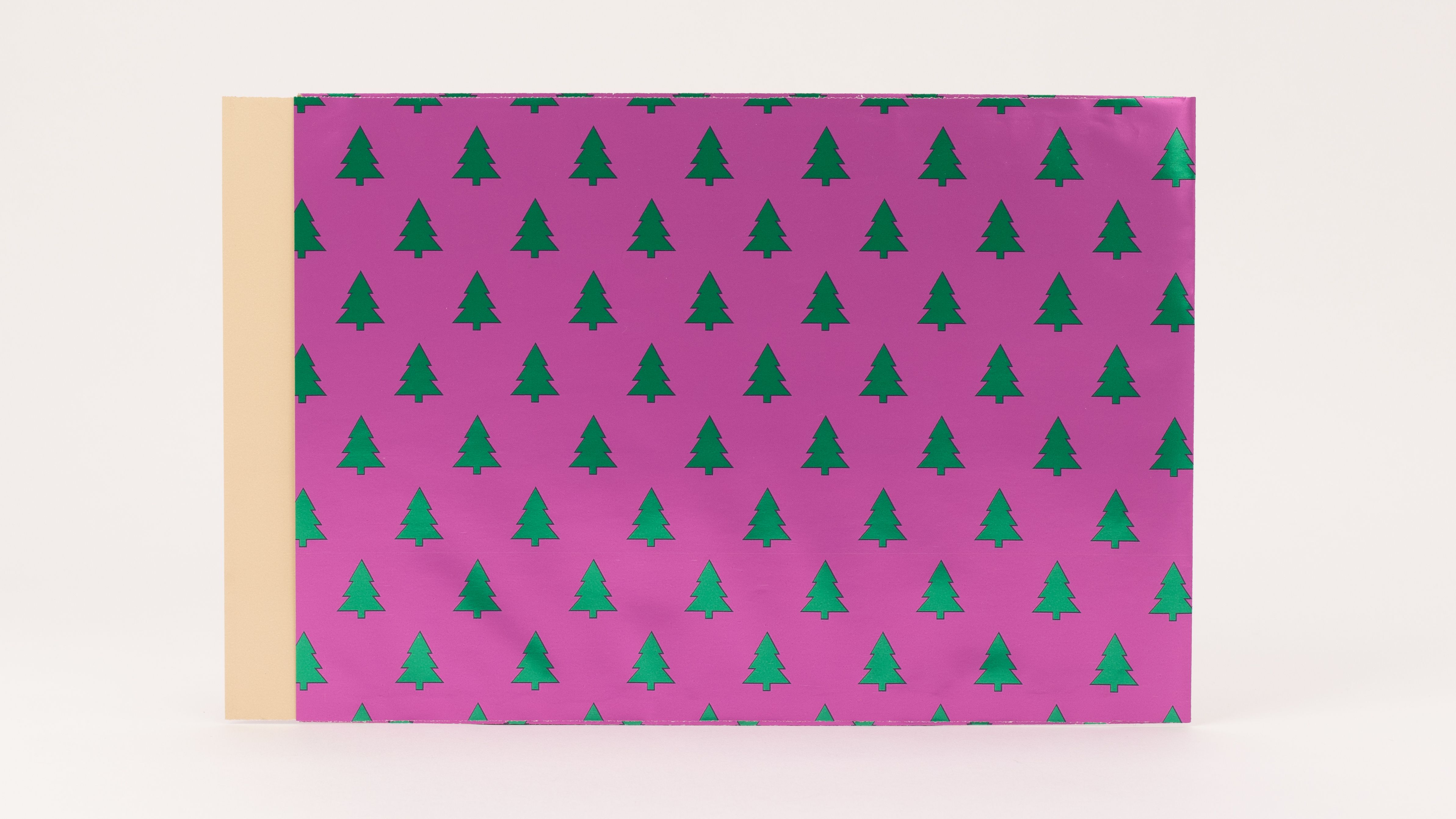 Flachbeutel mit pinker Außenseite und wiederholendem Muster aus grünen, metallisch glänzenden Tannenbäumen. Die Innenseite ist hellbraun.