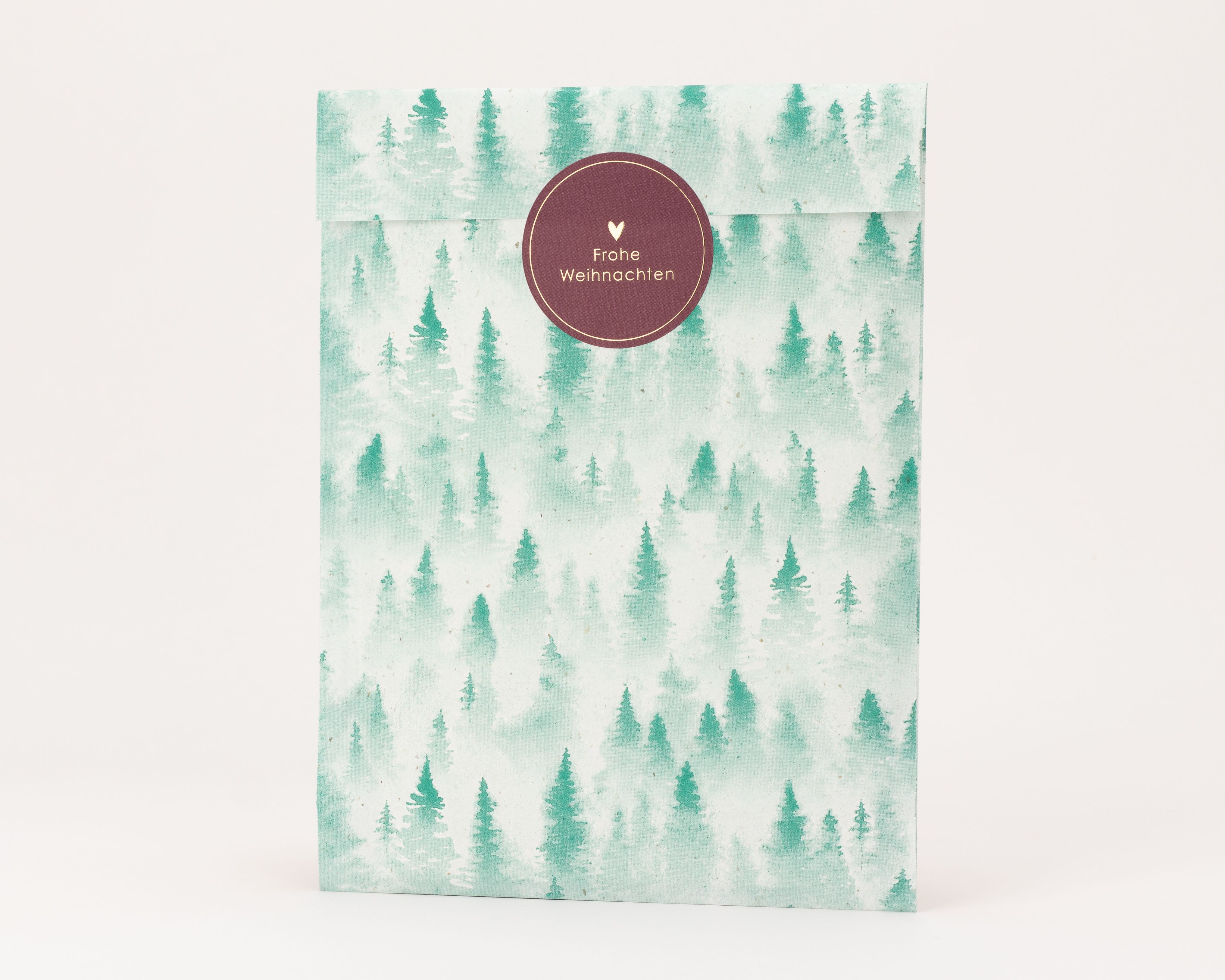 Papiertüten mit grünem Tannenwaldmuster auf hellem Grund und naturfarbener Innenseite, mit bordeauxrotem 'Frohe Weihnachten' Aufkleber