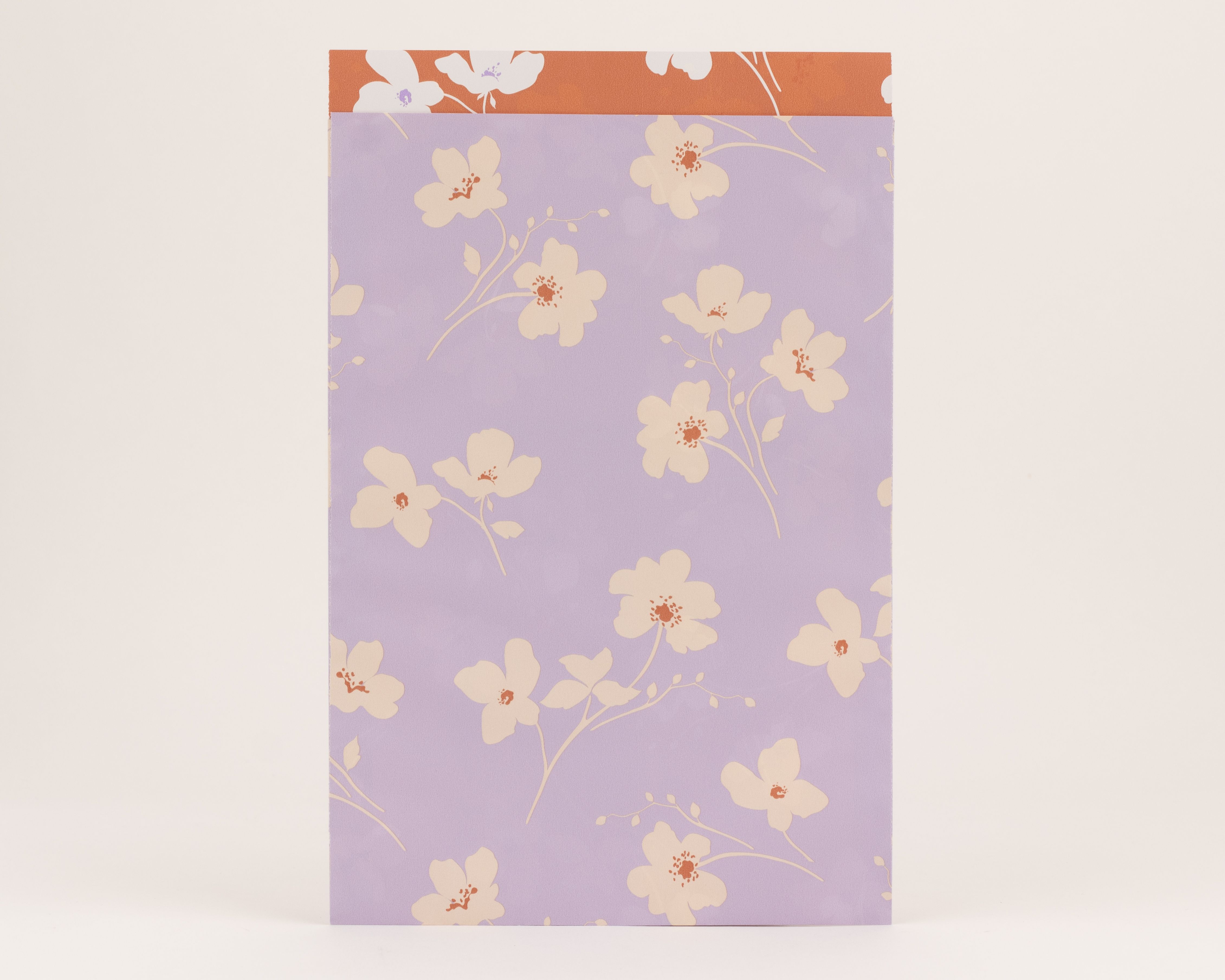 Flachbeutel in Flieder mit beigem Wiesenblütenmuster und rostfarbenen Details. Die Innenseite ist Rost mit beigem Blumenmuster