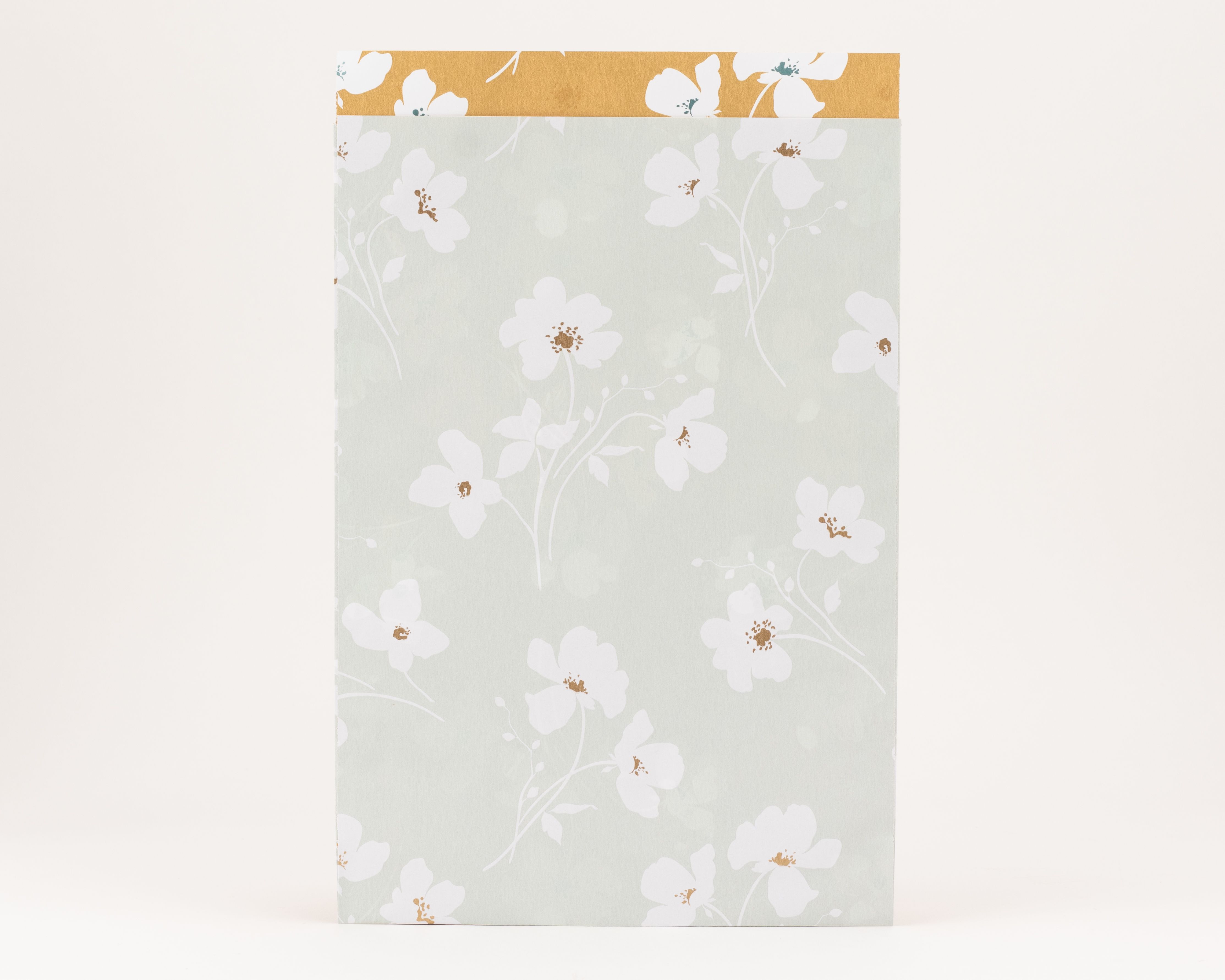 Flachbeutel in Salbeigrün mit weißem Wiesenblüten-Muster und goldenen Akzenten. Die Innenseite zeigt das gleiche Design auf ockerfarbenem Grund