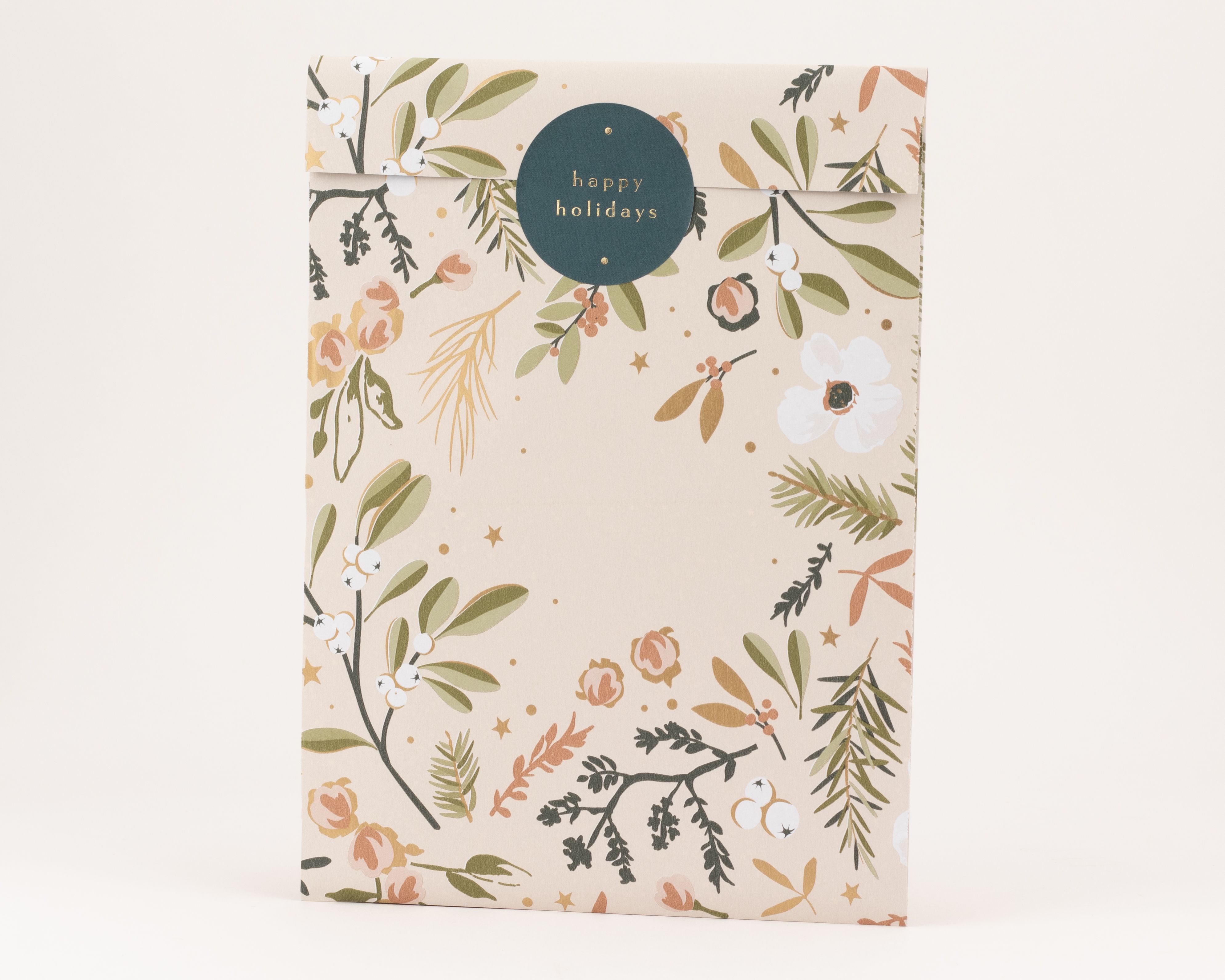 Flachbeutel in Blush Beige mit winterlichem Blumendesign und Goldeffekt. Ein petrolfarbener 'happy holidays' Aufkleber mit Goldtext