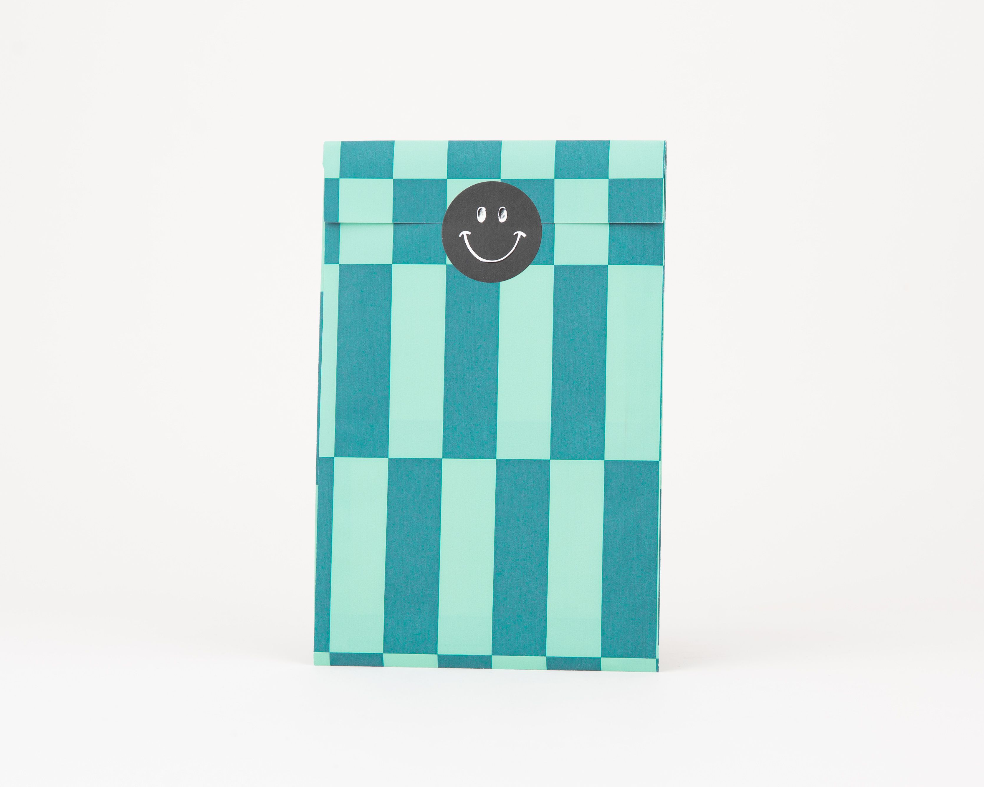 Papiertüten Flachbeutel in Blau und Grün mit Schachbrettmuster. Das Innere ist ebenfalls gemustert, ein schwarzer Smiley-Sticker ist auf dem Beutel