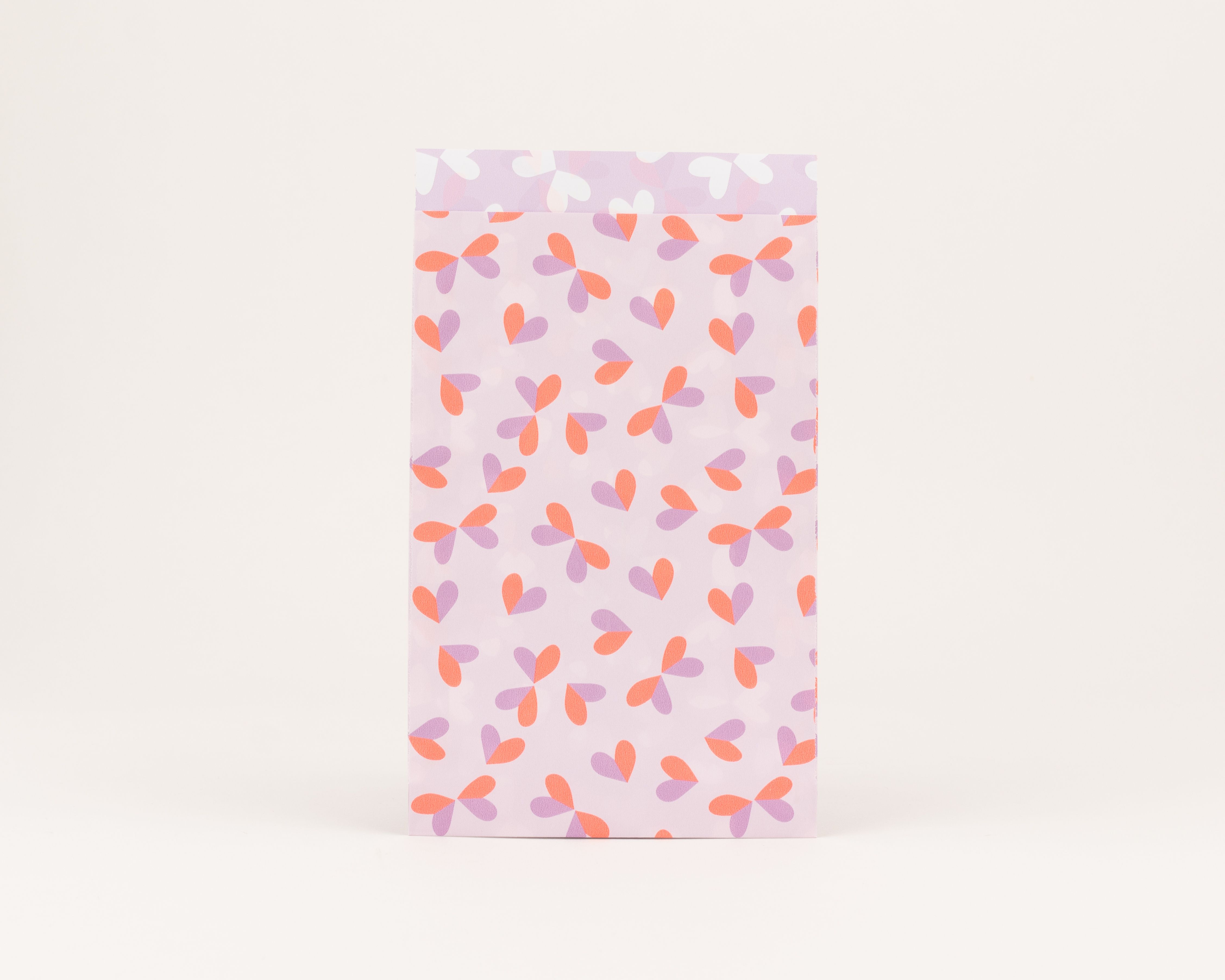 Flachbeutel mit hellfliederfarbenem Grund und Herzen in Hellflieder und Neon Orange. Die Innenseite zeigt weiße Herzen auf hellem Flieder