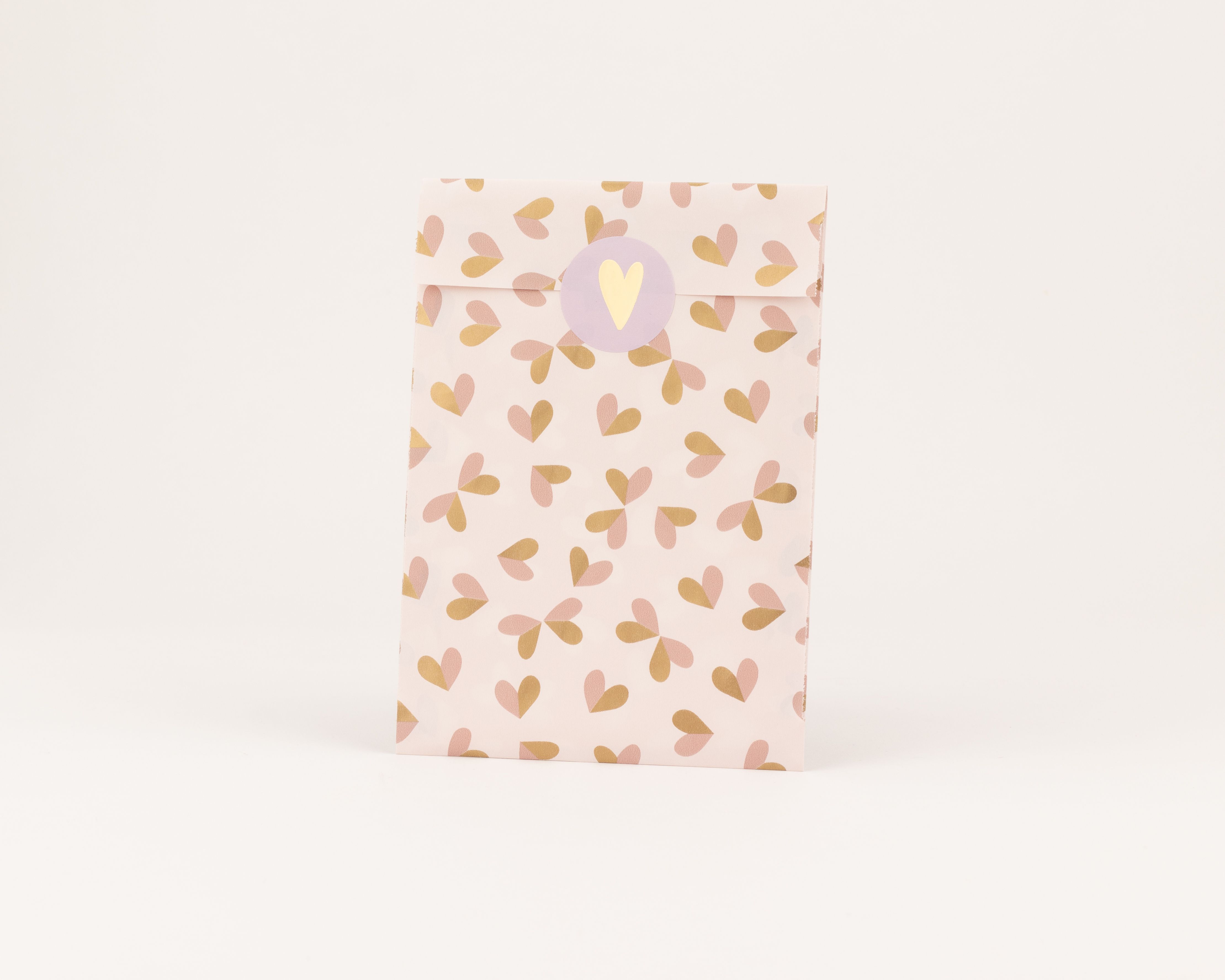 Papiertüten in Hellrosa mit Herzmuster in Rostbraun und Beige. Die Flachbeutel sind mit einem runden Aufkleber mit Herzmotiv geschlossen