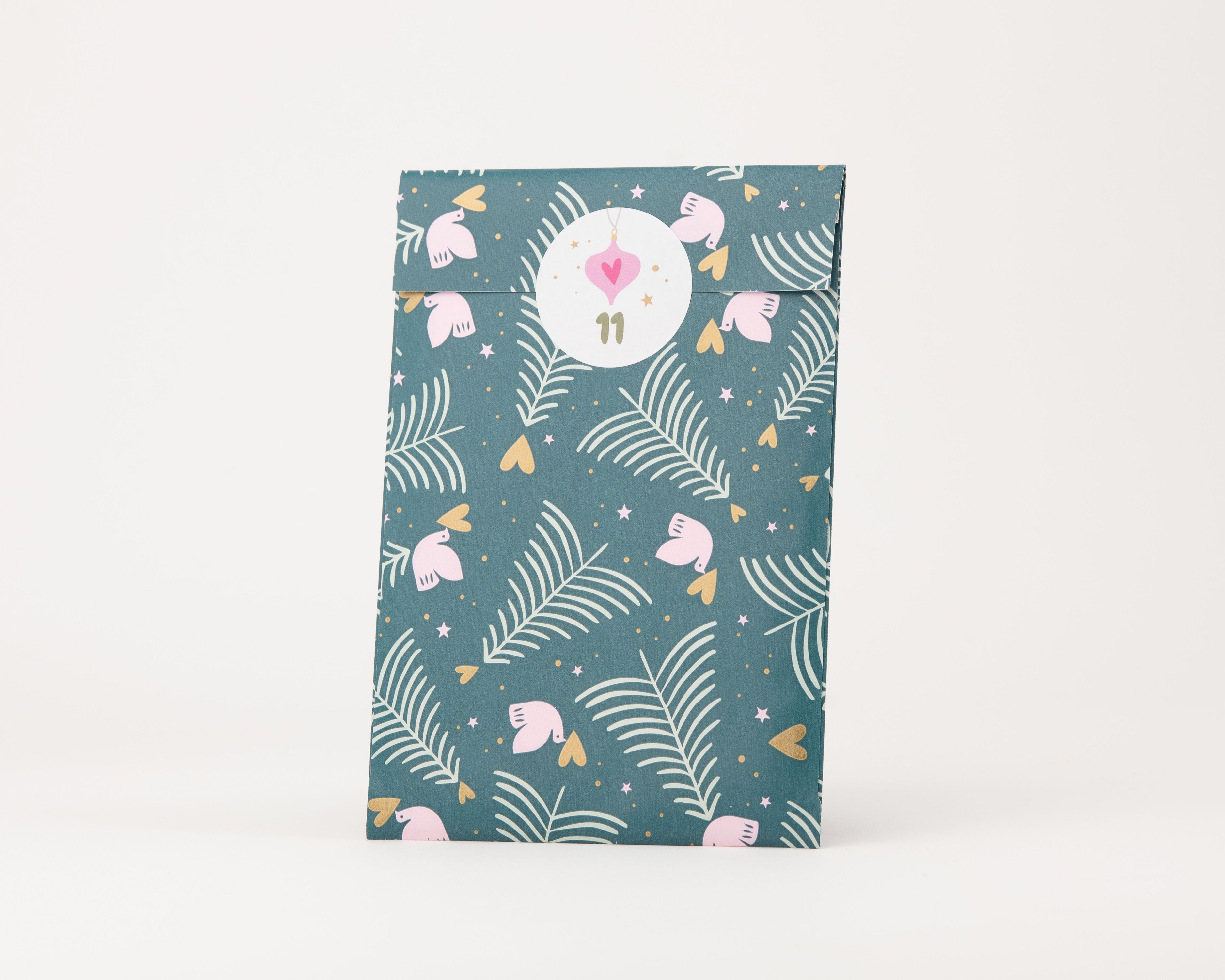 Papiertüten Flachbeutel zeigen ein Muster aus weißen Farnblättern, rosa Vögeln, goldenen Herzen und kleinen Sternen auf einem petrolfarbenen Hintergrund