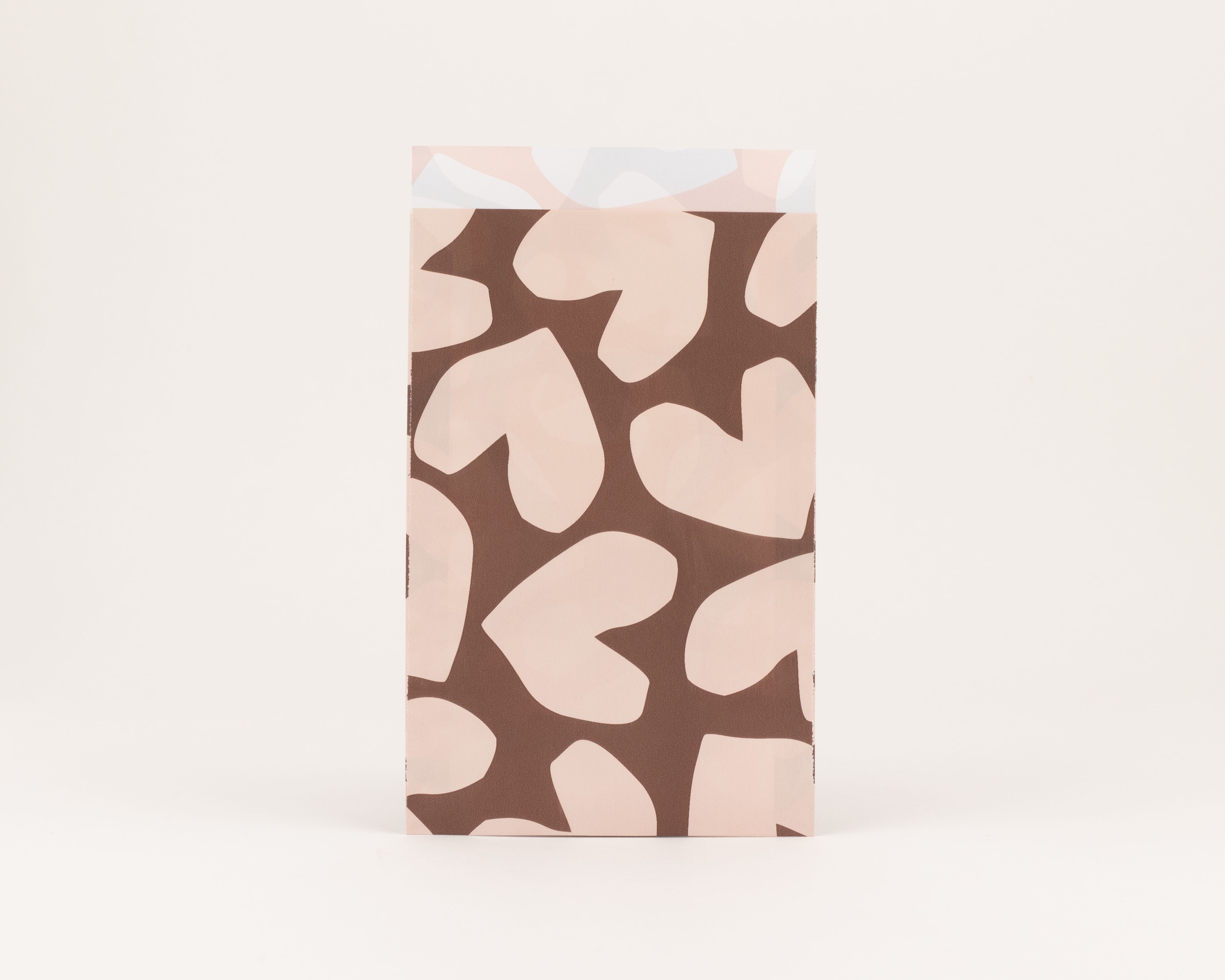 Flachbeutel mit einem Muster aus beigen Herzen auf braunem Grund. Die sichtbare Innenseite der Tüte ist beige und weist leichte, abstrakte Muster auf