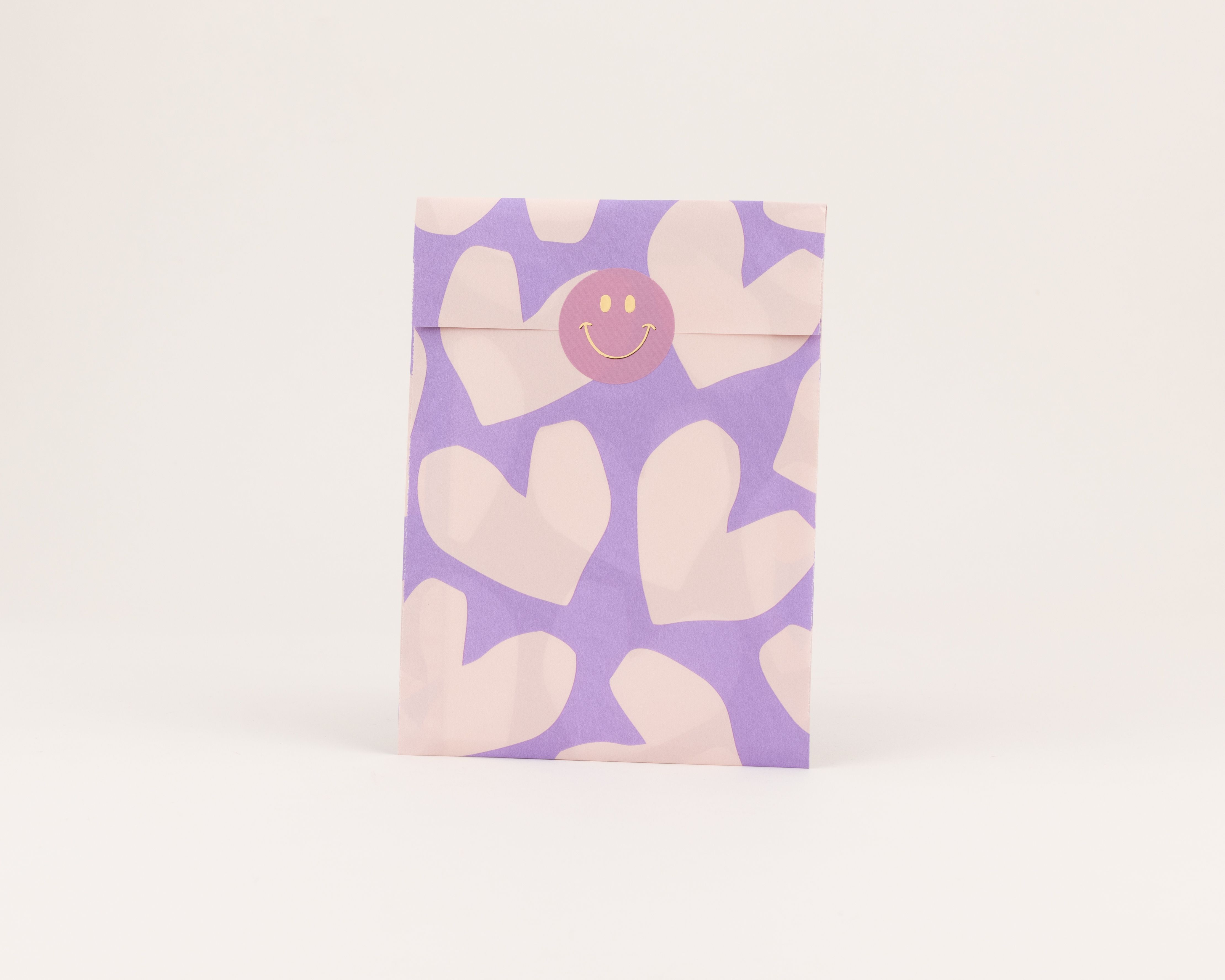 Flachbeutel mit einem Muster aus hellfliederfarbenen Herzen auf lila Außenseite und einer hellfliederfarbenen Innenseite mit Smiley-Sticker