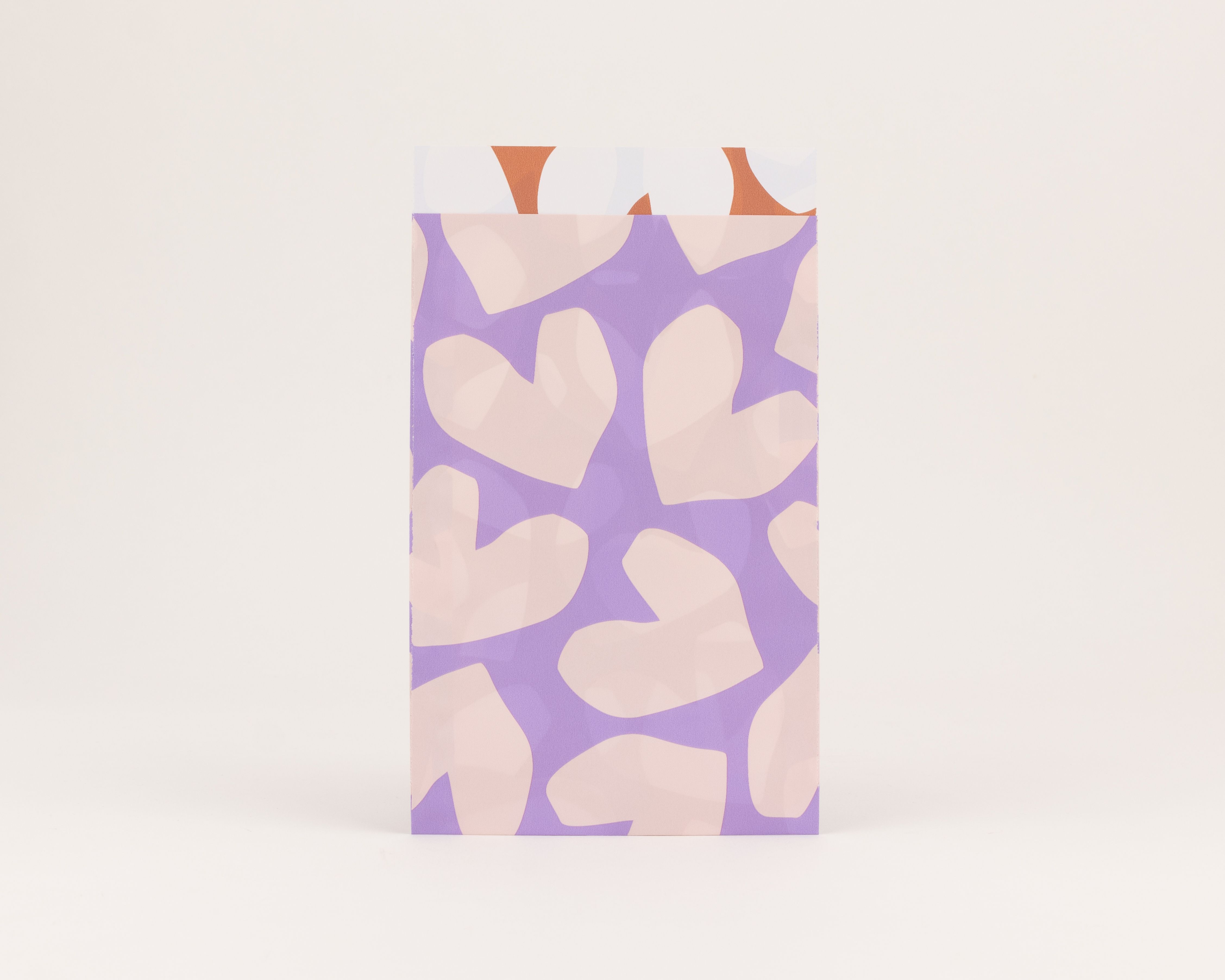 Flachbeutel mit lila Außenseite und hellfliederfarbenem Herzmuster. Die Innenseite zeigt rostige und weiße Formen auf hellem Grund