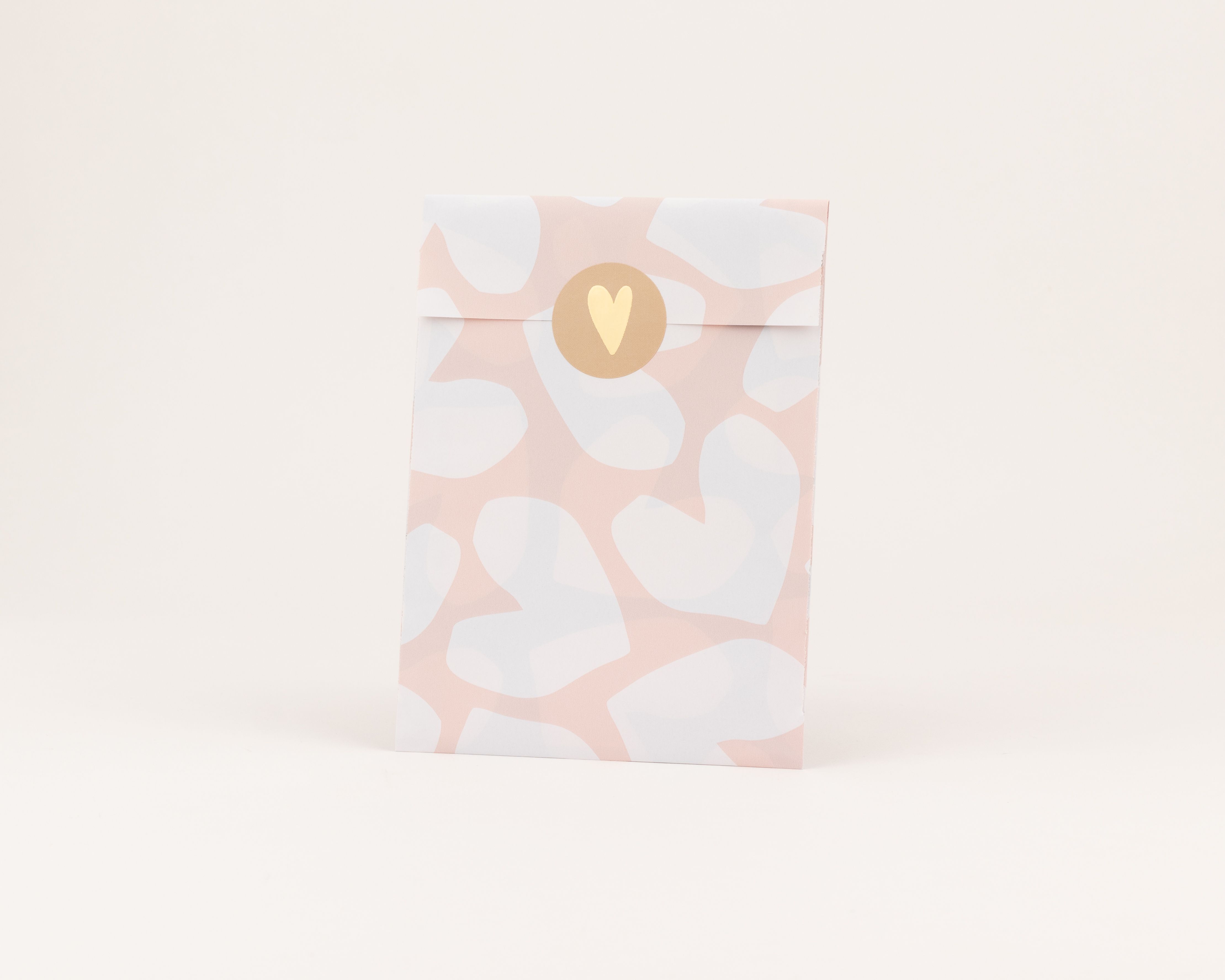 Papiertüten mit rosa und weißen Herzen als Muster, geschlossen mit einem runden braunen Sticker mit goldener Herzprägung und sichtbarer weißer Innenseite