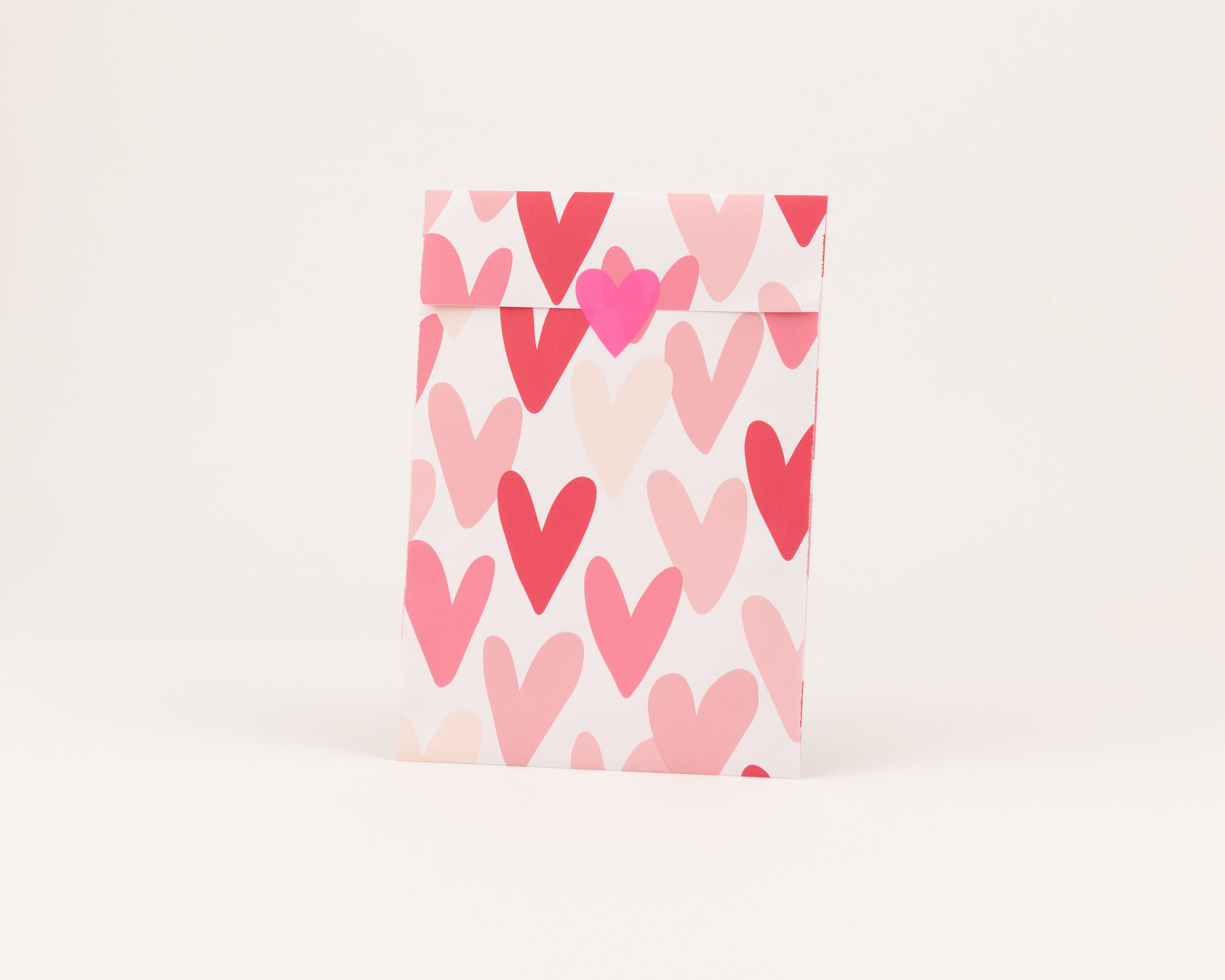Flachbeutel mit einem Muster aus Herzen in Pink, Rosa und hellem Beige auf der Außenseite, wobei die Innenseite einfarbig pink ist