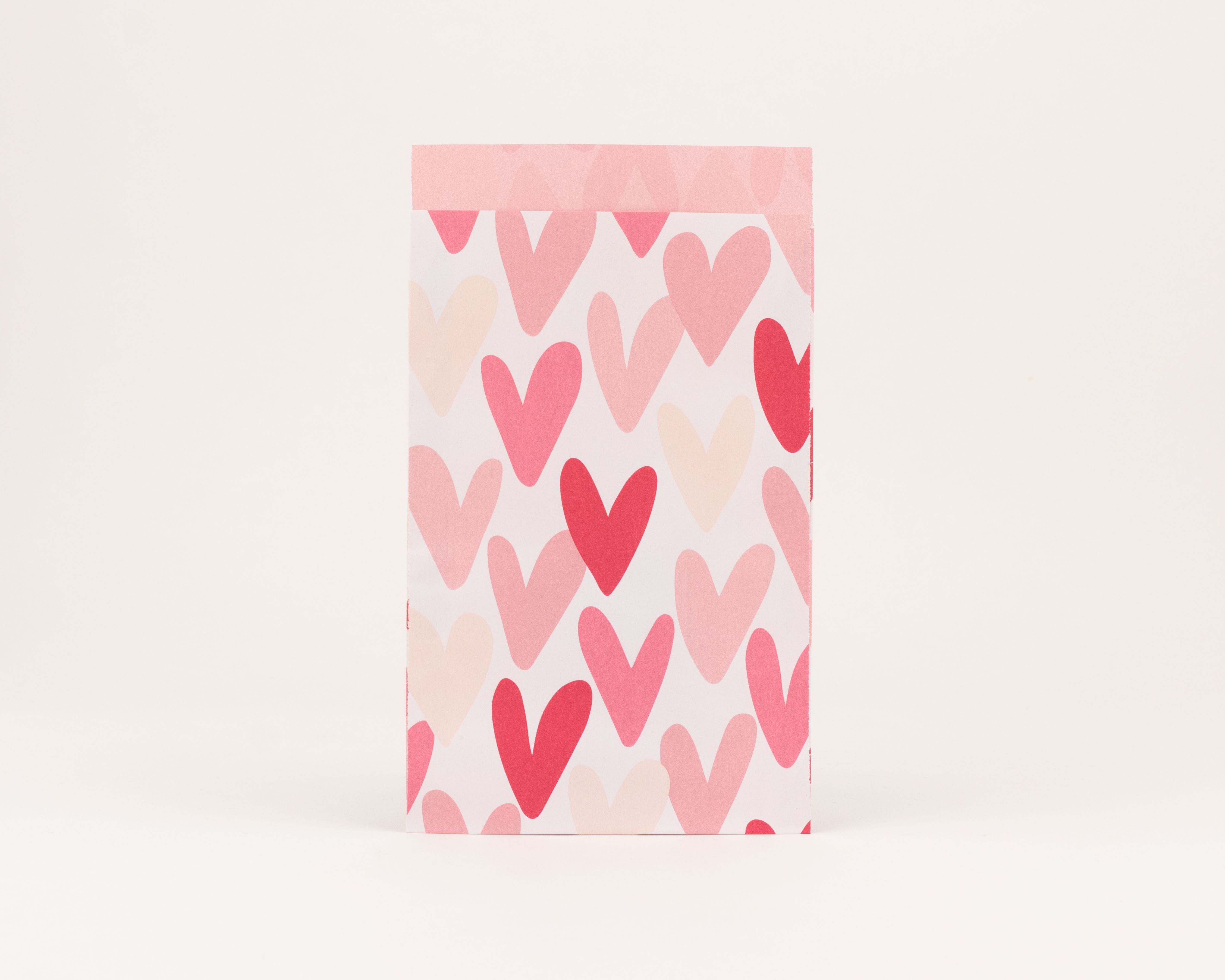 Flachbeutel mit einem Muster aus pinken, rosa und beigen Herzen auf der Außenseite und einer einfarbig pinken Innenseite