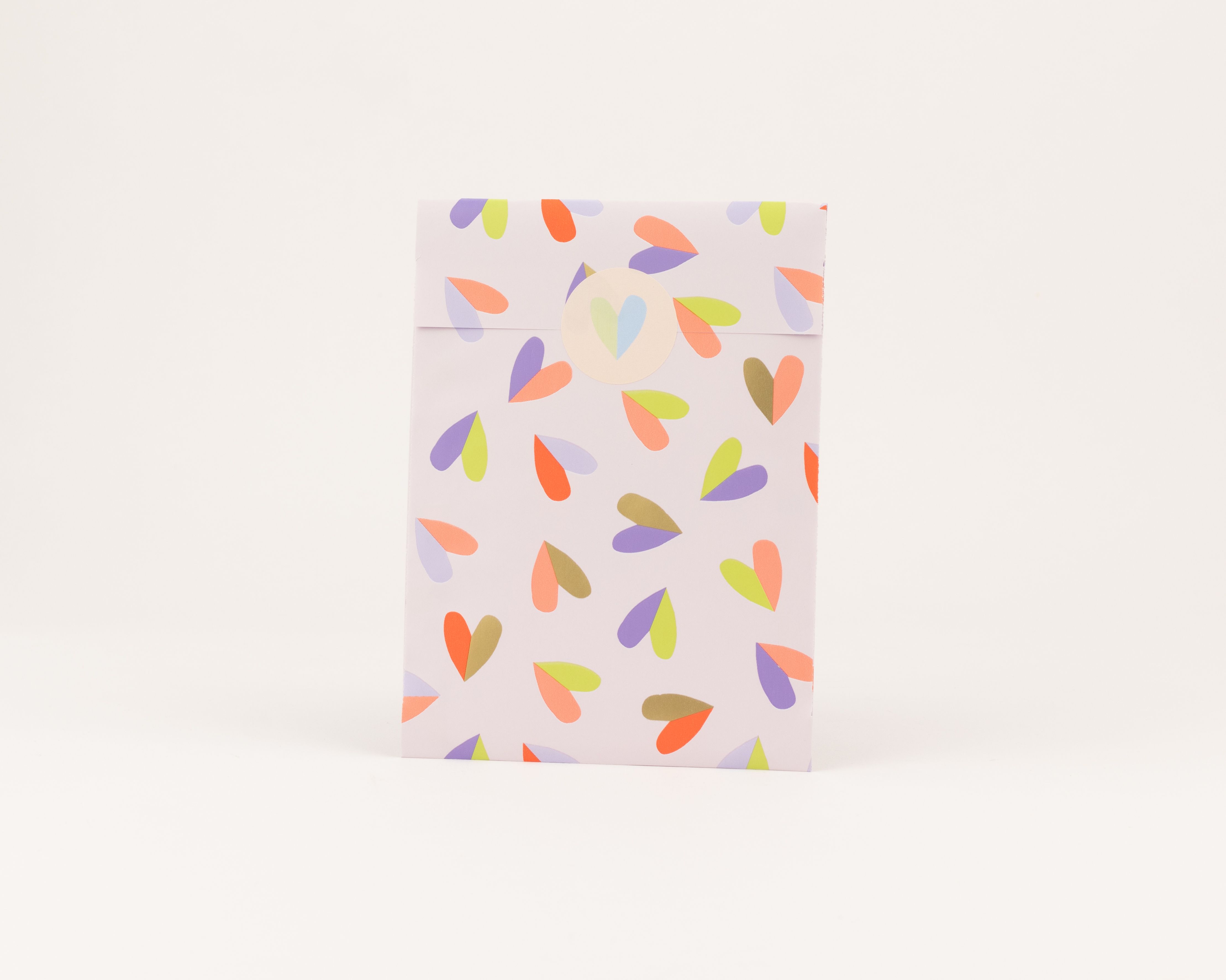 Flachbeutel mit fliederfarbener Außenseite und Herzmuster in Orange, Violett, Limettengrün, Hellviolett. Die Innenseite ist Hellviolett