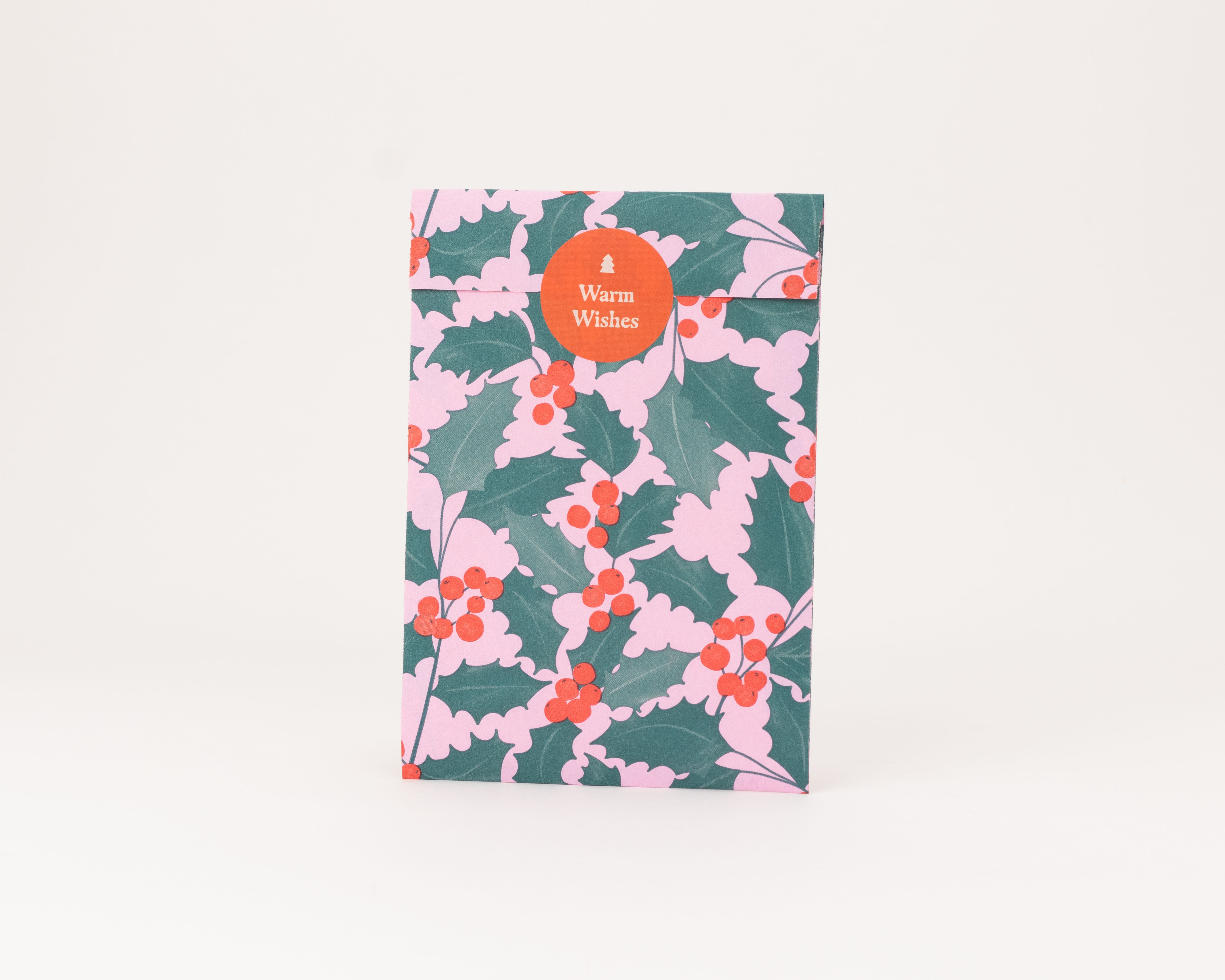 Flachbeutel mit Ilex-Design in Rosa, Grün und Rot, die Innenseite ist ebenfalls Rosa und ein runder orangefarbener Aufkleber